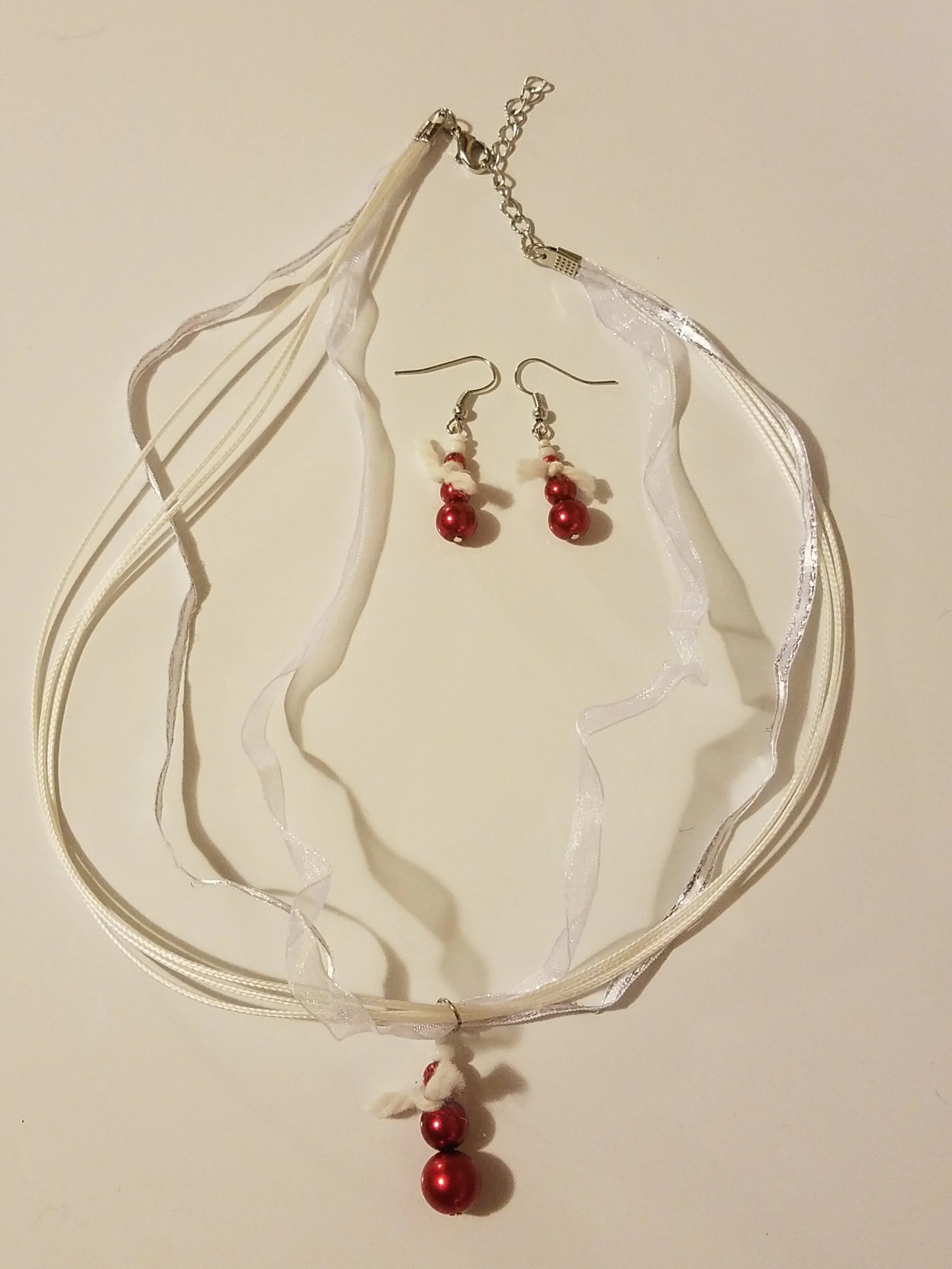 Red pearl jewelry set including a necklace with white ribbons and a charm, and matching earrings with red pearls and white beads.