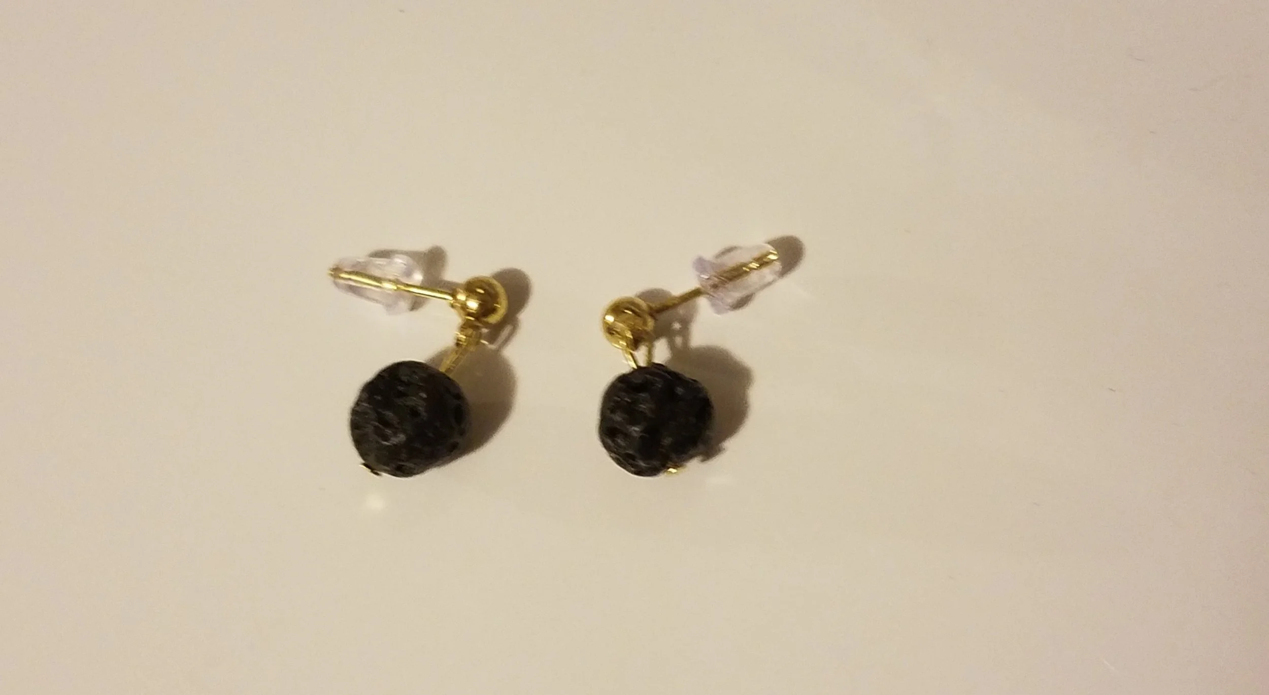Pair of gold and black stud earrings with round black stones on a white background.