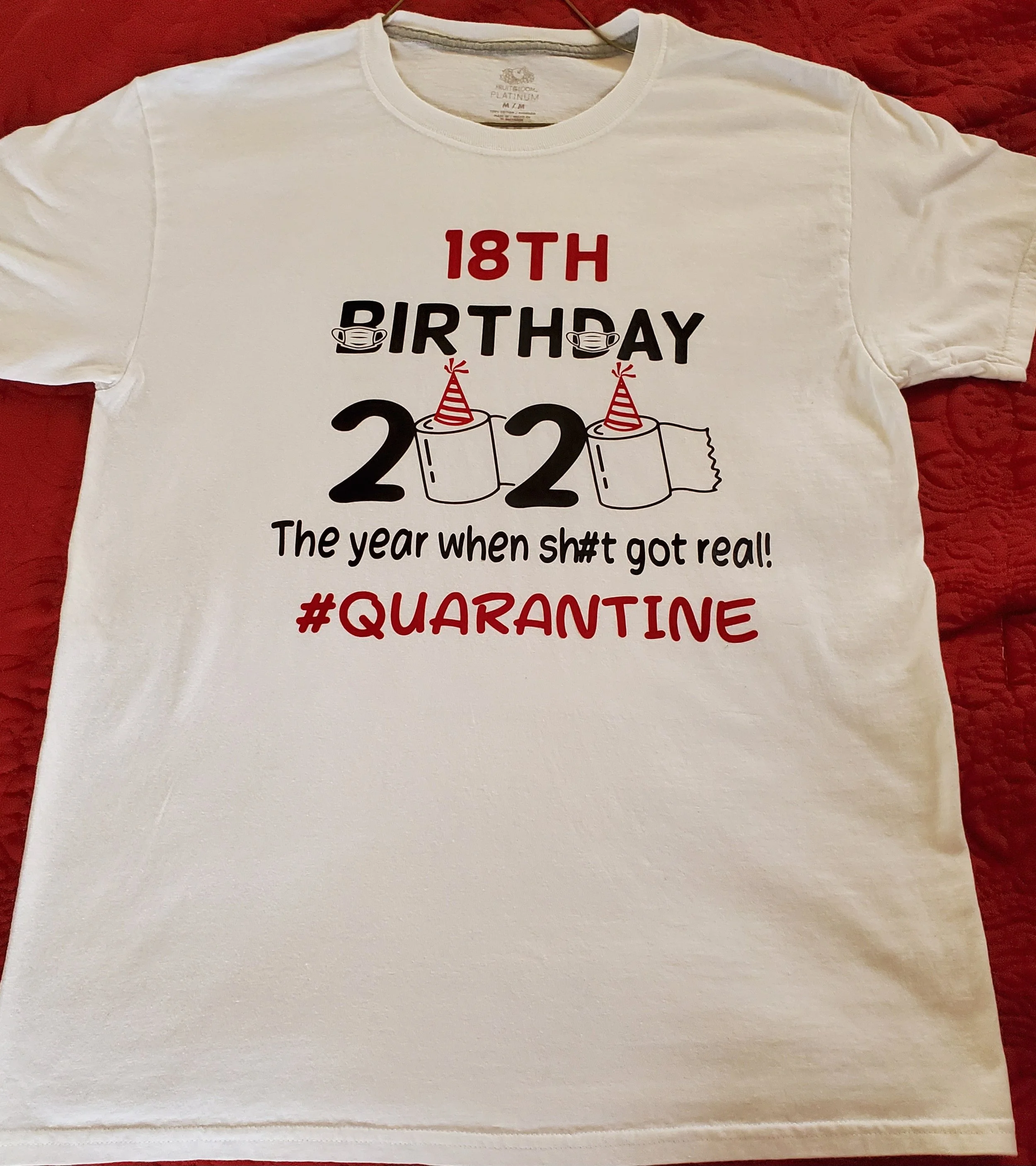 White T-shirt with red and black text celebrating an 18th birthday in 2022 during quarantine, with illustrations of face masks and party hats.