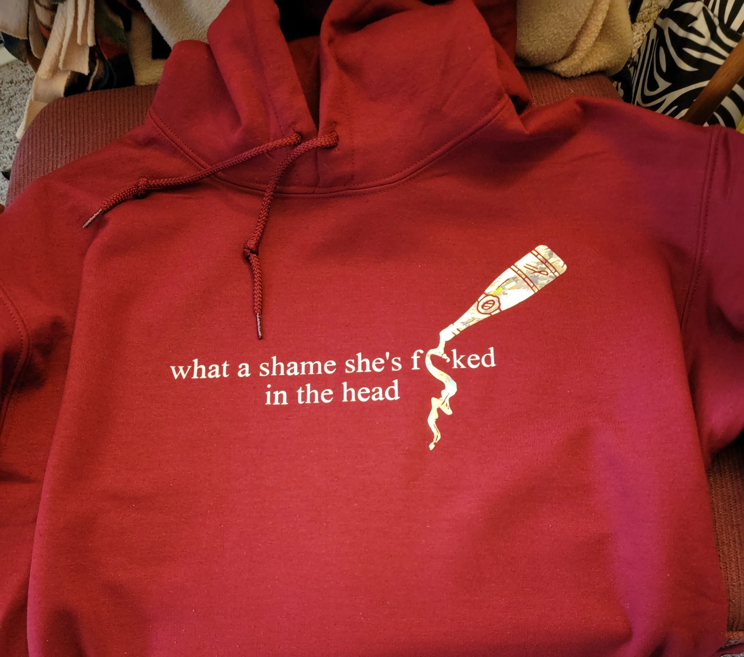 Red hoodie with a cigarette illustration and the text "what a shame she's f**ked in the head" printed on it.