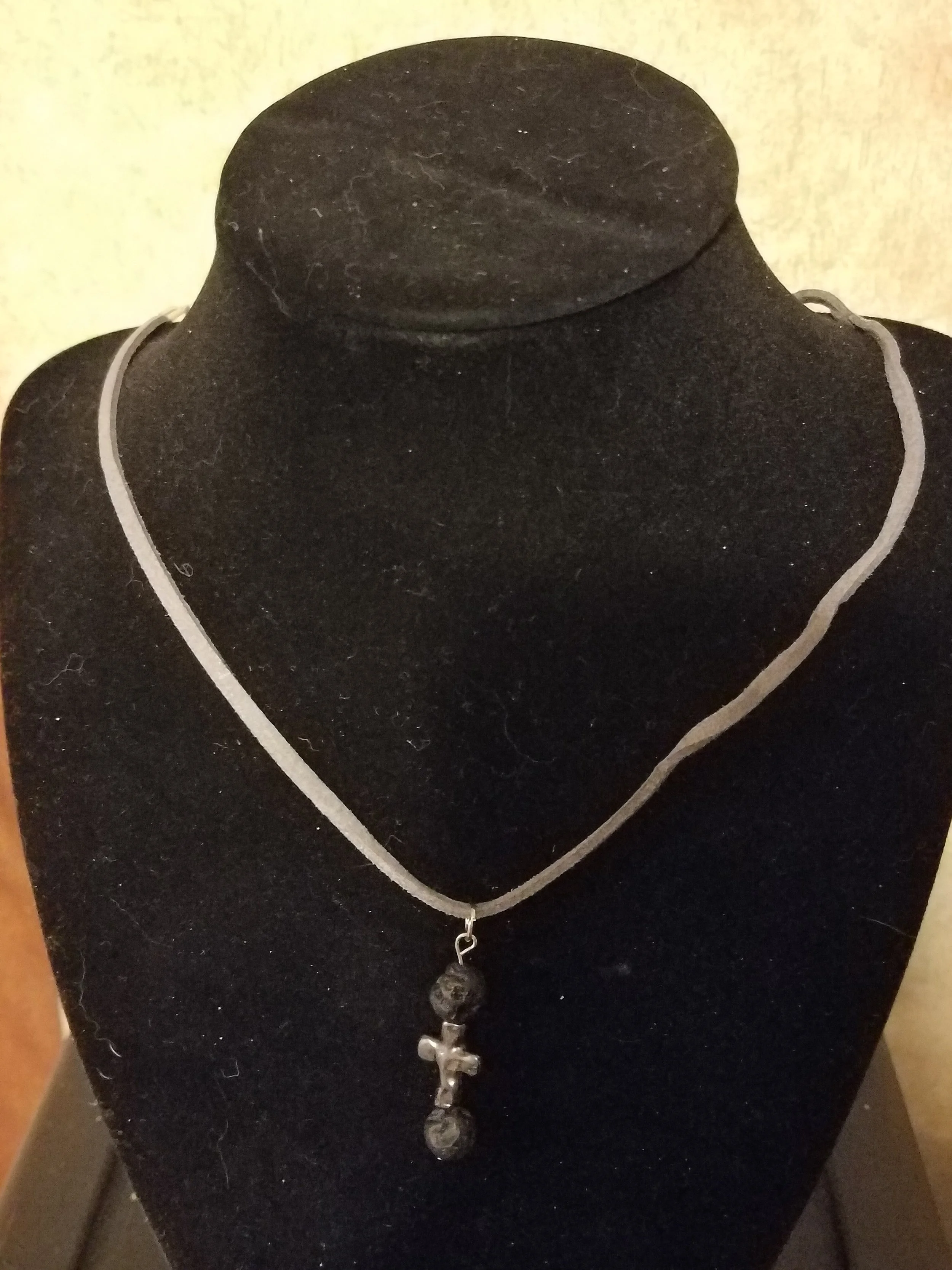 A necklace displayed on a black jewelry stand with a cross pendant and beaded design.