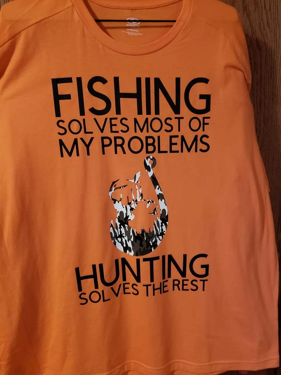 Orange T-shirt with black text and camouflage deer silhouette. The text reads: 'FISHING SOLVES MOST OF MY PROBLEMS. HUNTING SOLVES THE REST.'