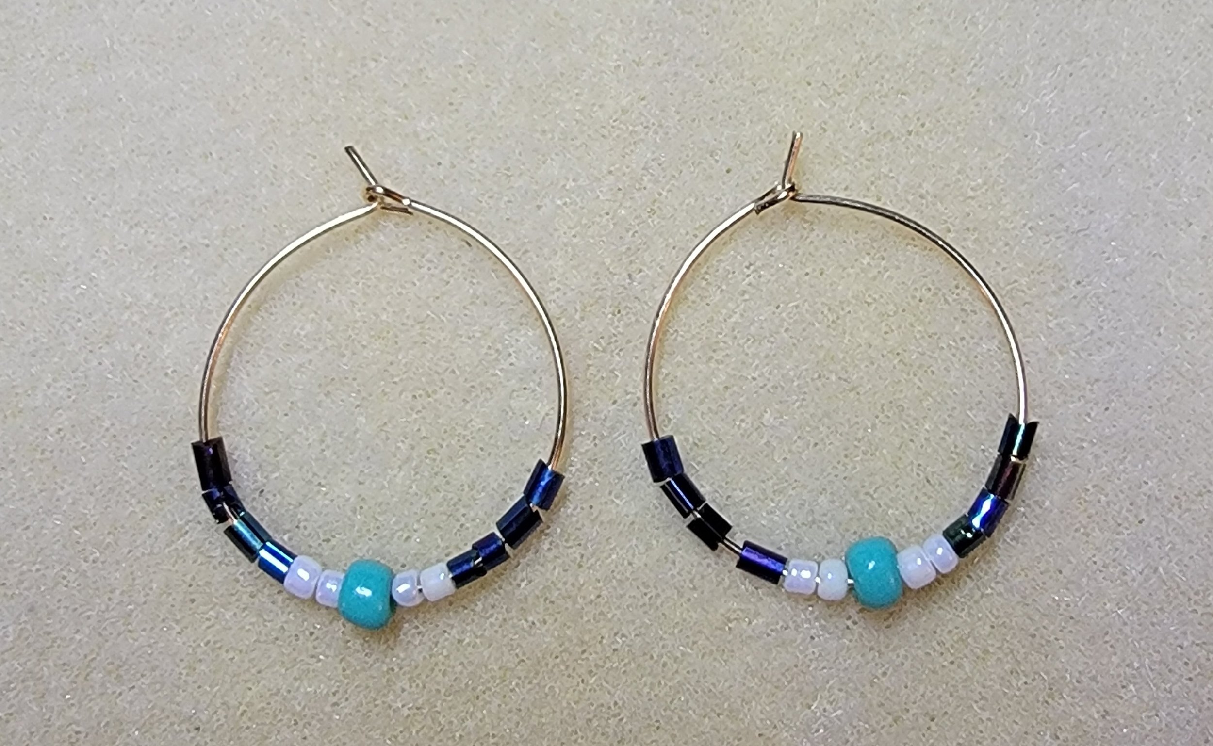 Pair of beaded hoop earrings with blue and white beads on a beige background.