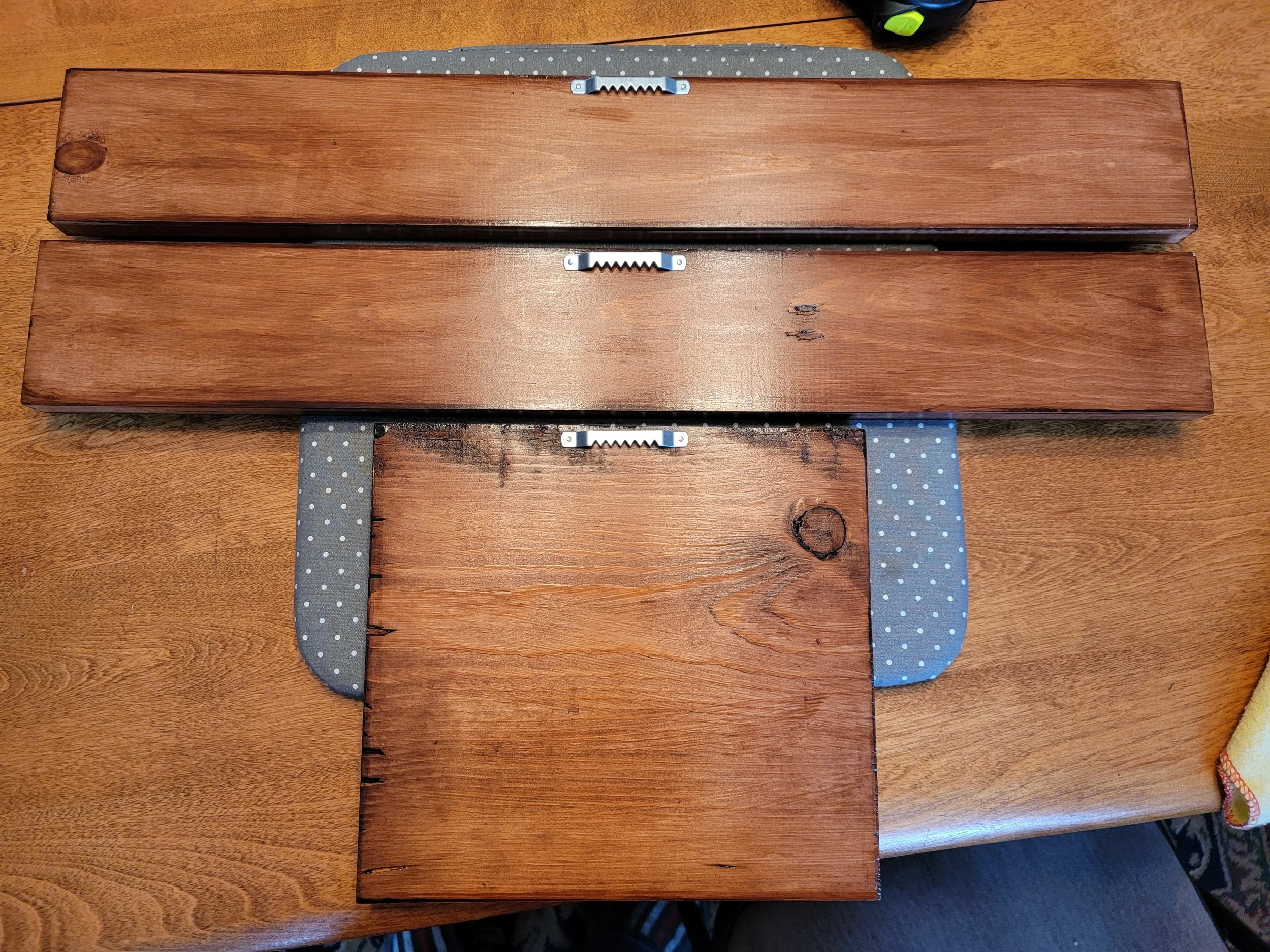 Three wooden planks placed on a polka dot fabric on a wood table, with a gray item in the top right corner.