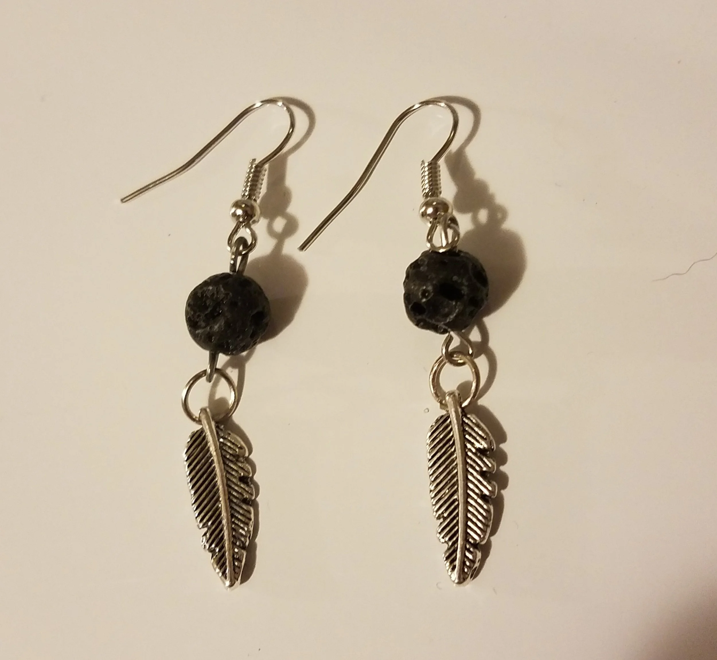 Pair of silver earrings with black beads and feather charms on a white background.