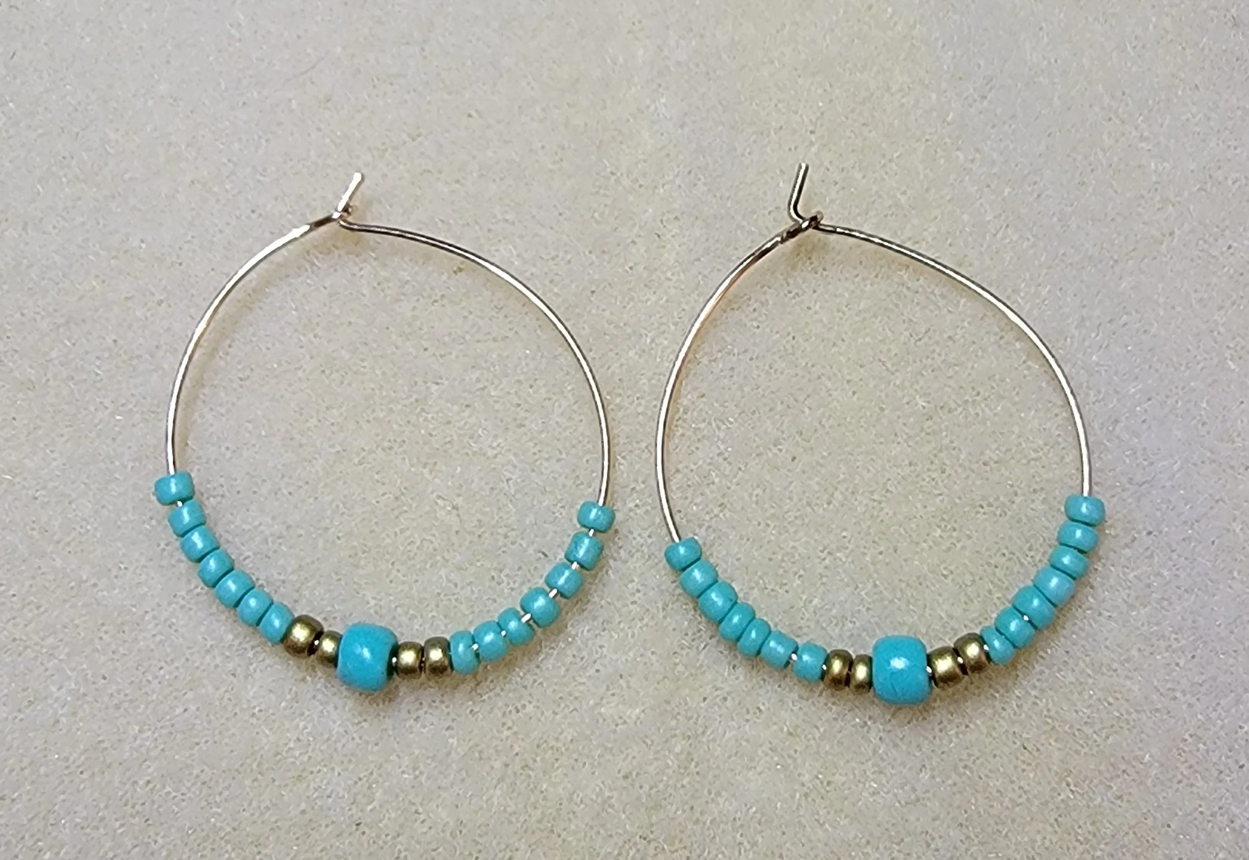 Silver hoop earrings with turquoise and gold beads on a light background.