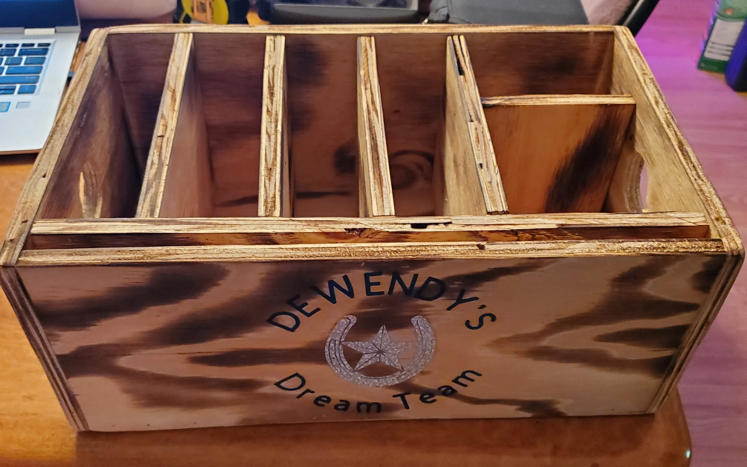 Wooden crate with separated compartments, decorated with the words "DeWendy's Dream Team" and a star and horseshoe emblem.