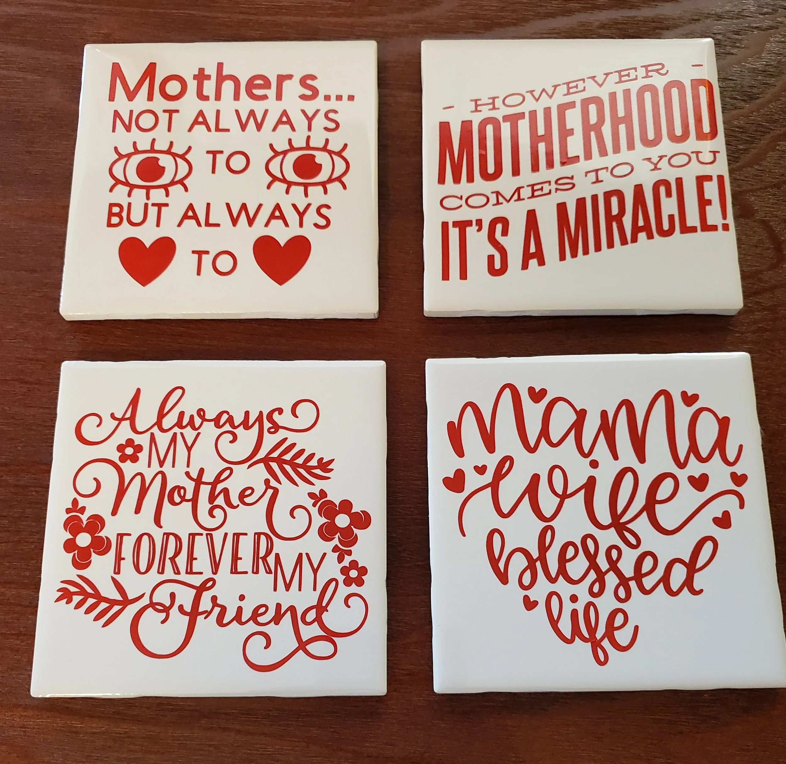 Four white decorative tiles with red text and designs about motherhood and family, arranged in a 2x2 grid.