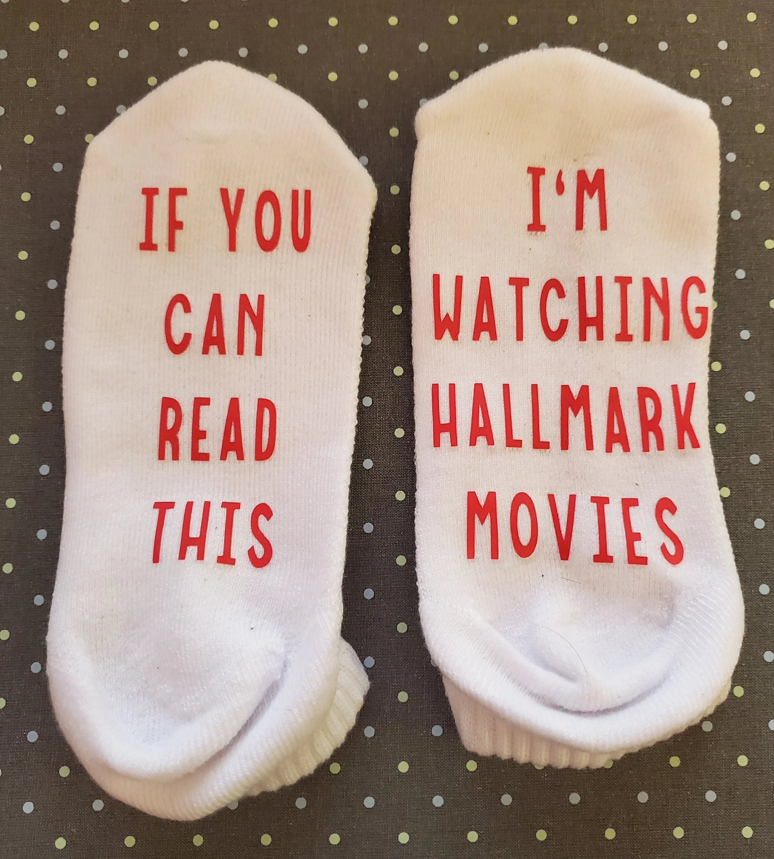 White socks with red text; one says 'IF YOU CAN READ THIS' and the other says 'I'M WATCHING HALLMARK MOVIES'.