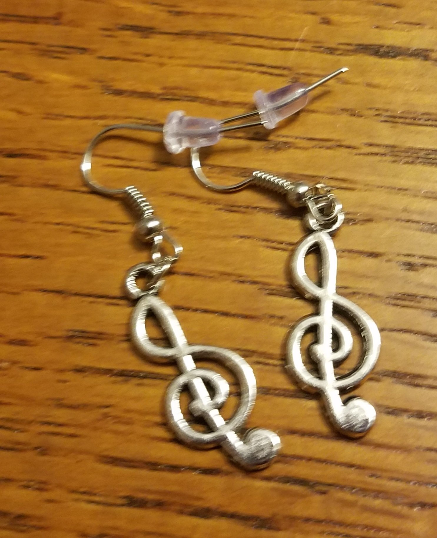 Pair of dangling earrings with treble clef musical note design on a wooden surface.