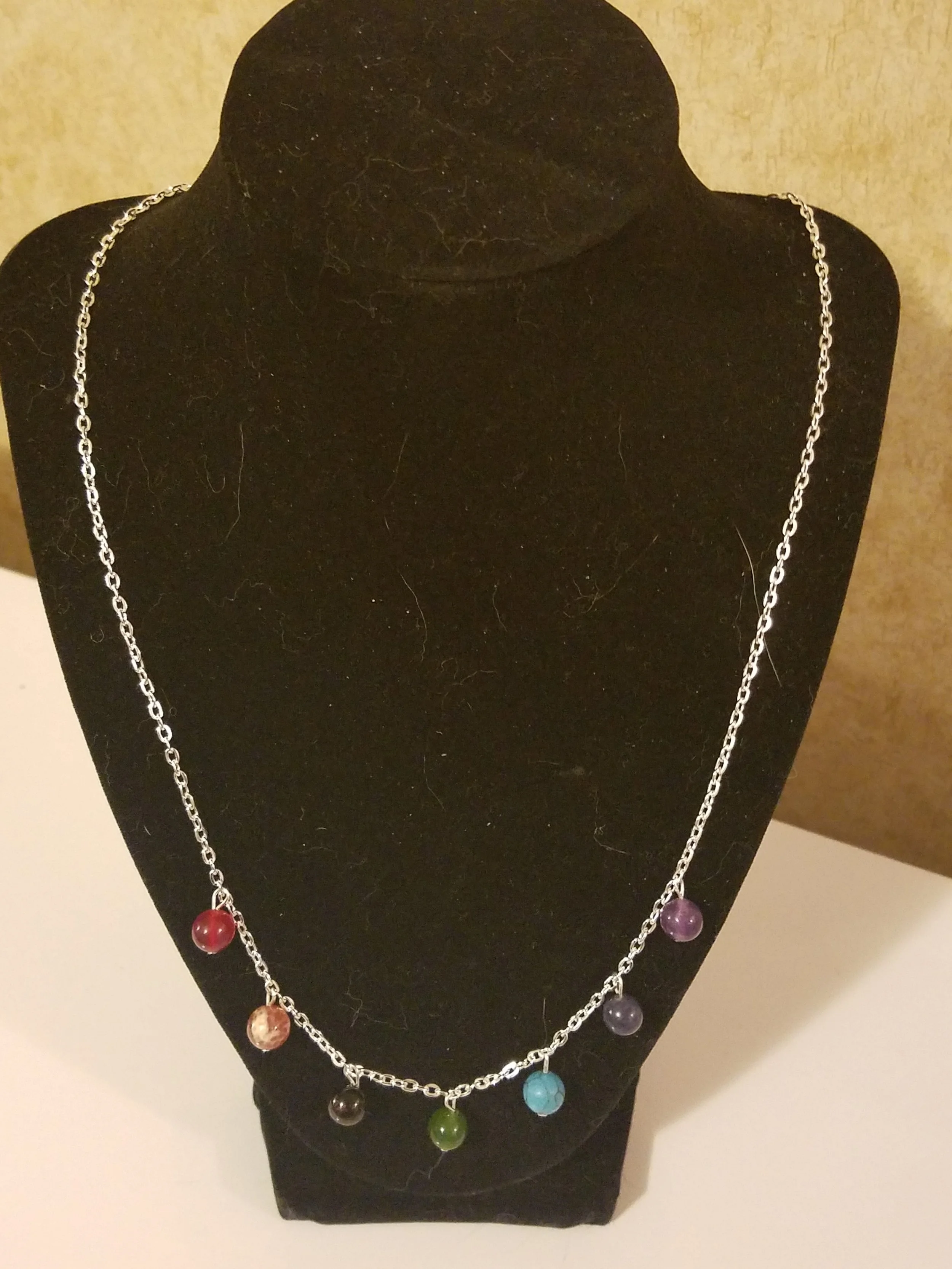 Silver necklace with multiple round colorful beads displayed on a black velvet jewelry stand.