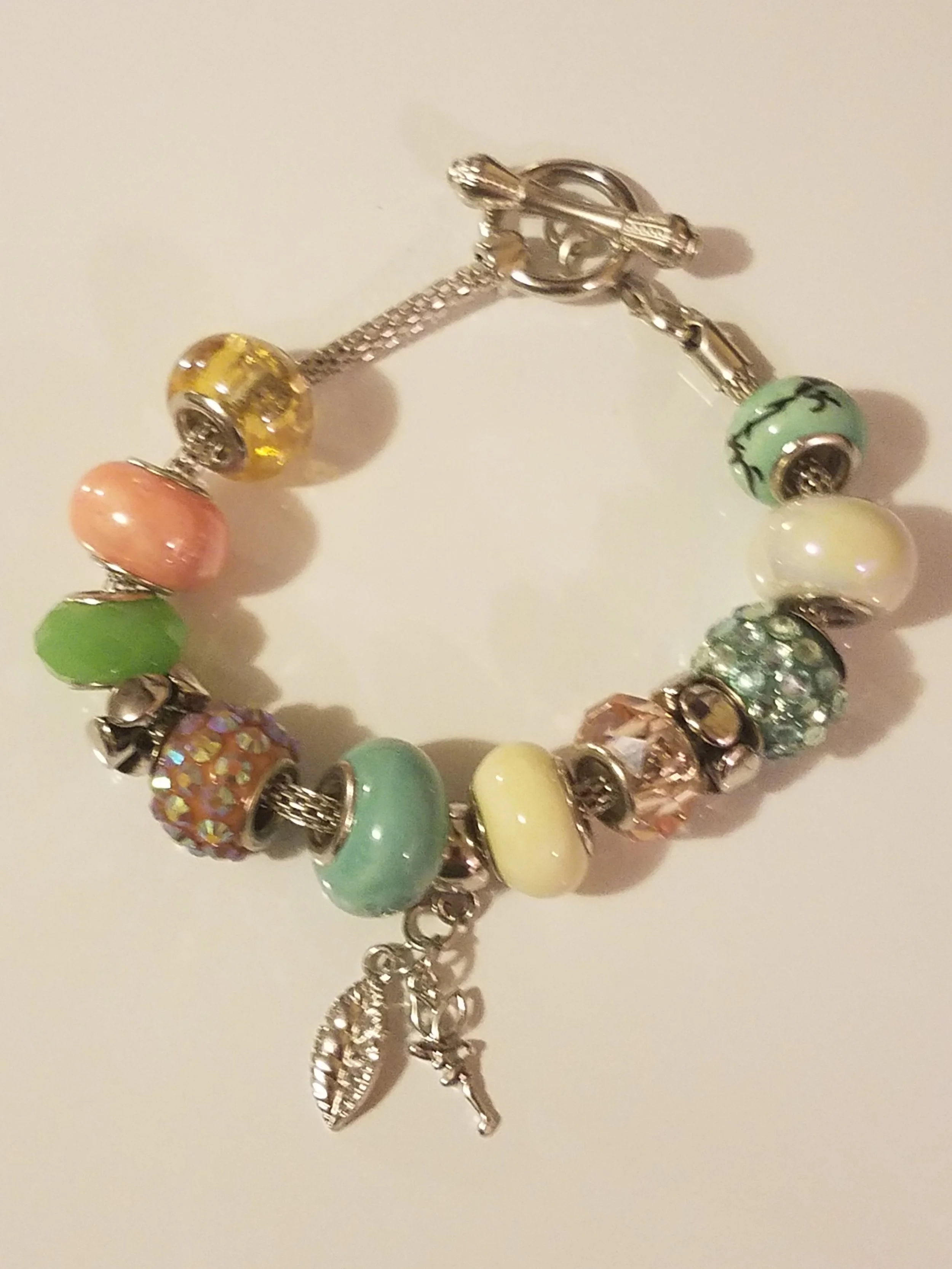 Colorful charm bracelet with various beads and small charms, including a feather and a high heel, on a white background.
