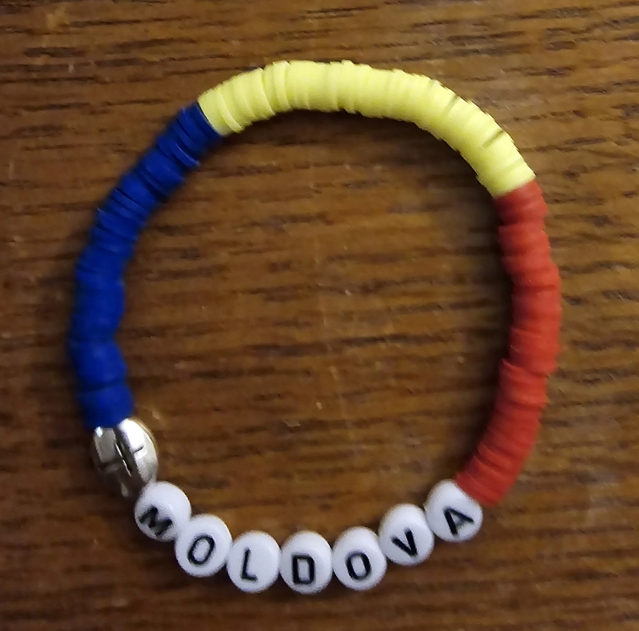Colorful beaded bracelet with the name 'MOLDOVA' spelled out on letter beads, placed on a wooden surface.