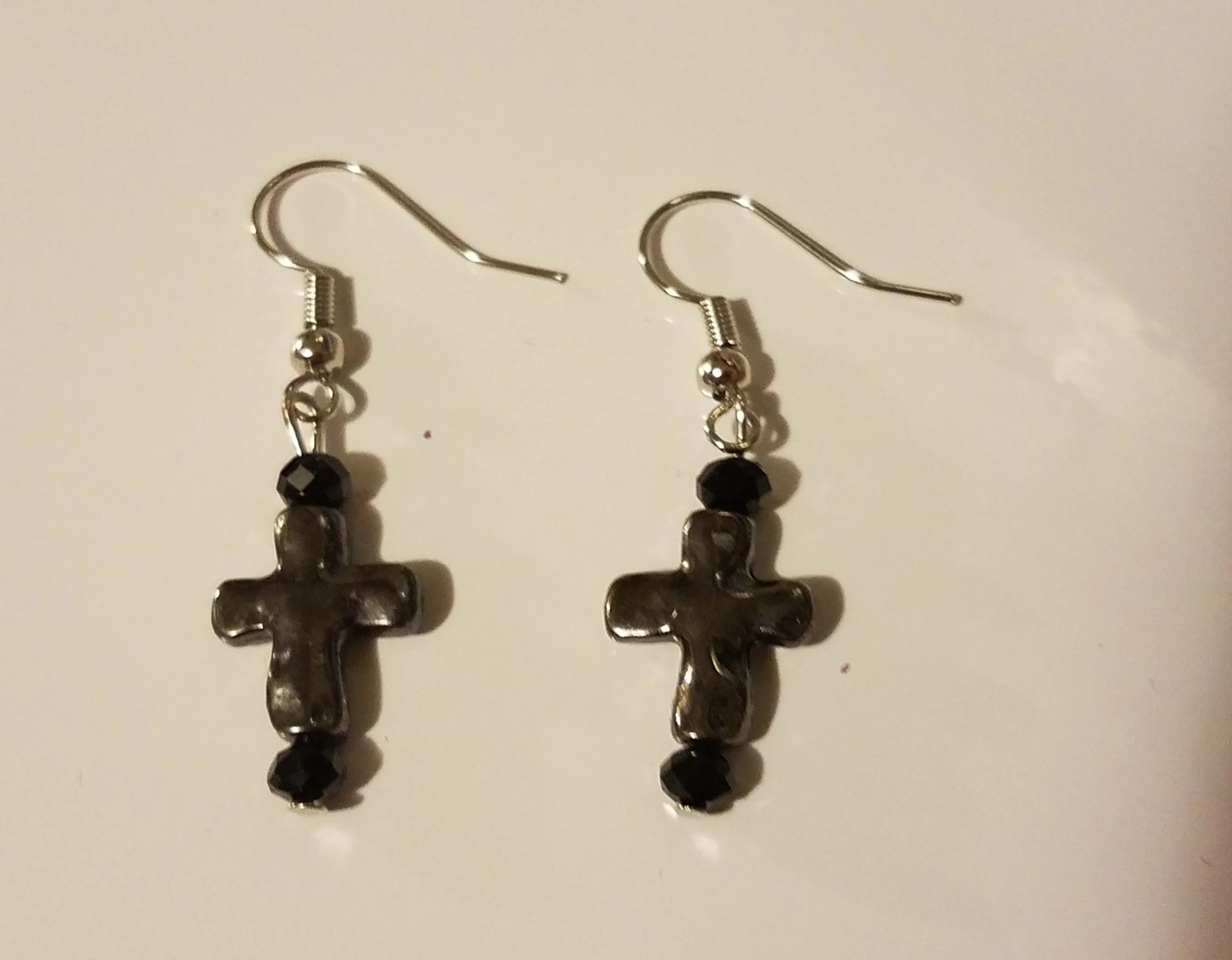 Pair of earrings with black beads and metallic cross charms, hanging from silver hooks.