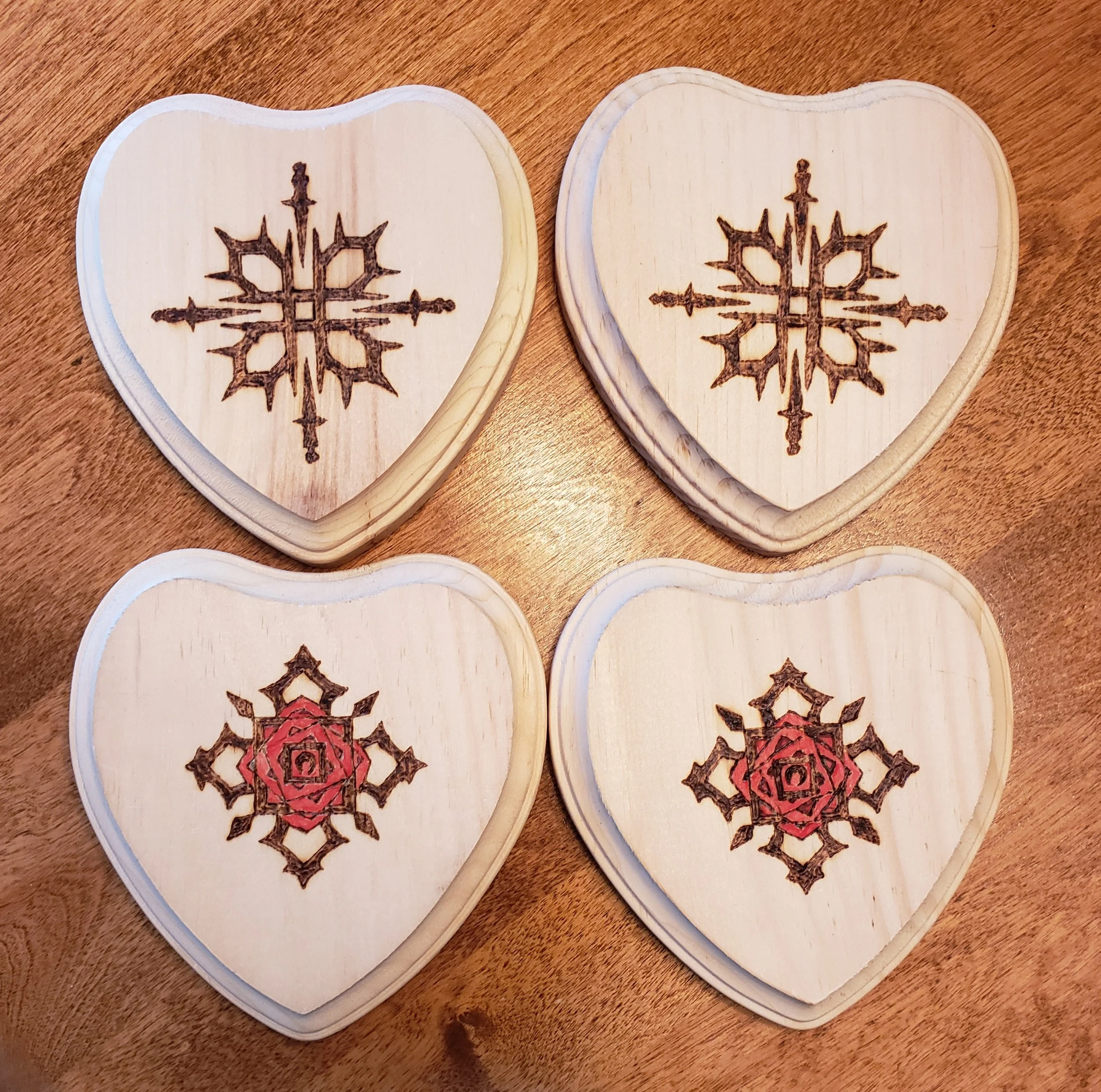 Four wooden heart-shaped coasters with intricate laser engravings, two with a snowflake pattern in dark brown and two with a red floral or geometric pattern.