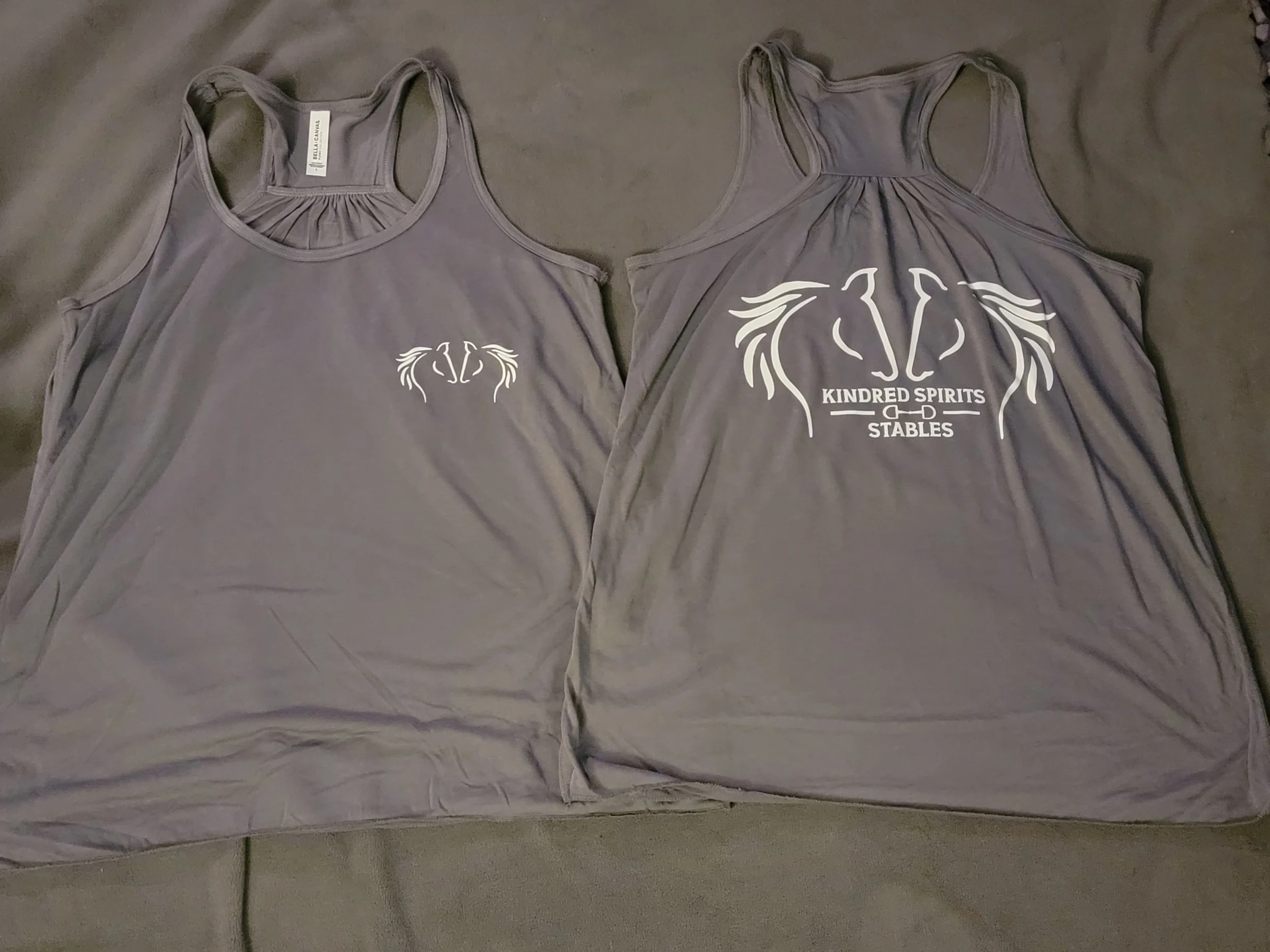 Two gray tank tops with horse-themed logos placed on a dark surface.