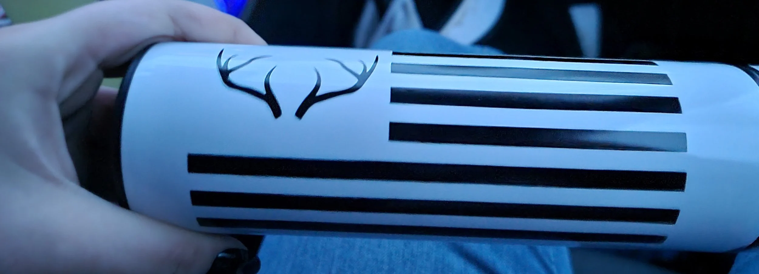 Hand holding a cylindrical container with a black antler logo and black horizontal stripes.