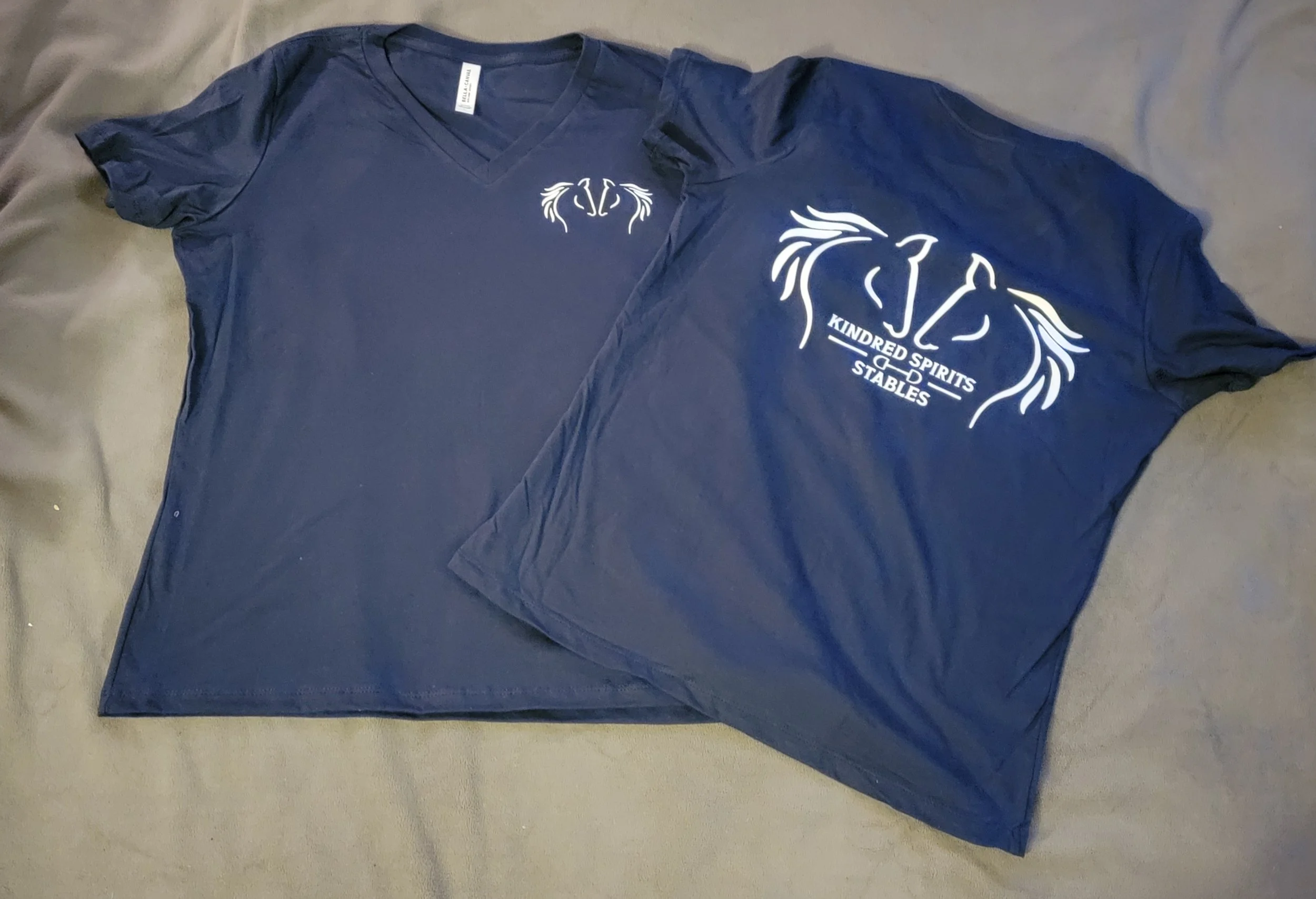 A navy blue T-shirt and matching pillowcase, each with a white logo featuring a stylized horse head and the text 'Kindred Spirits Stables' underneath.