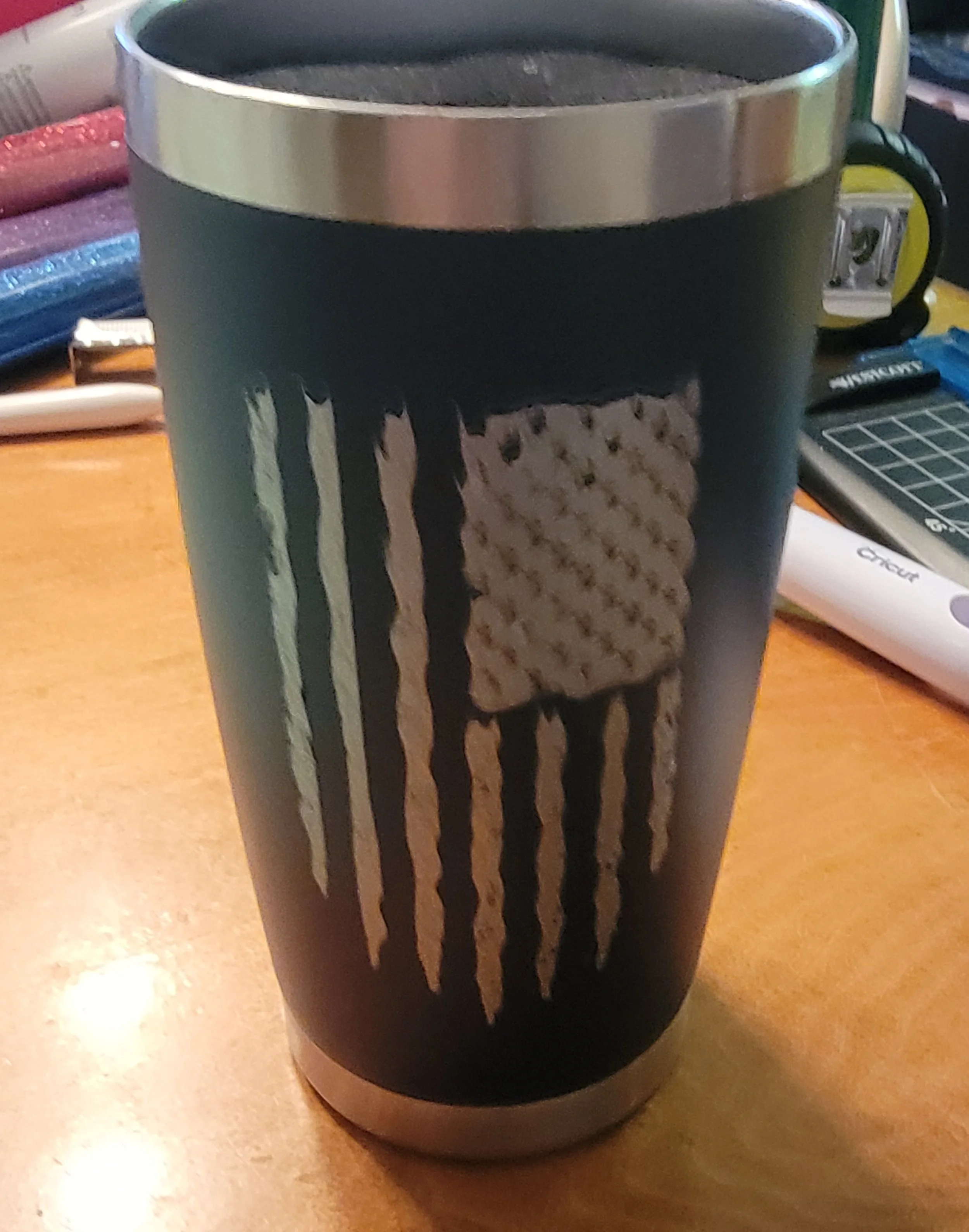 Travel mug with Monster Energy logo on a wooden desk surrounded by notebooks, pens, a tape measure, and a calculator.