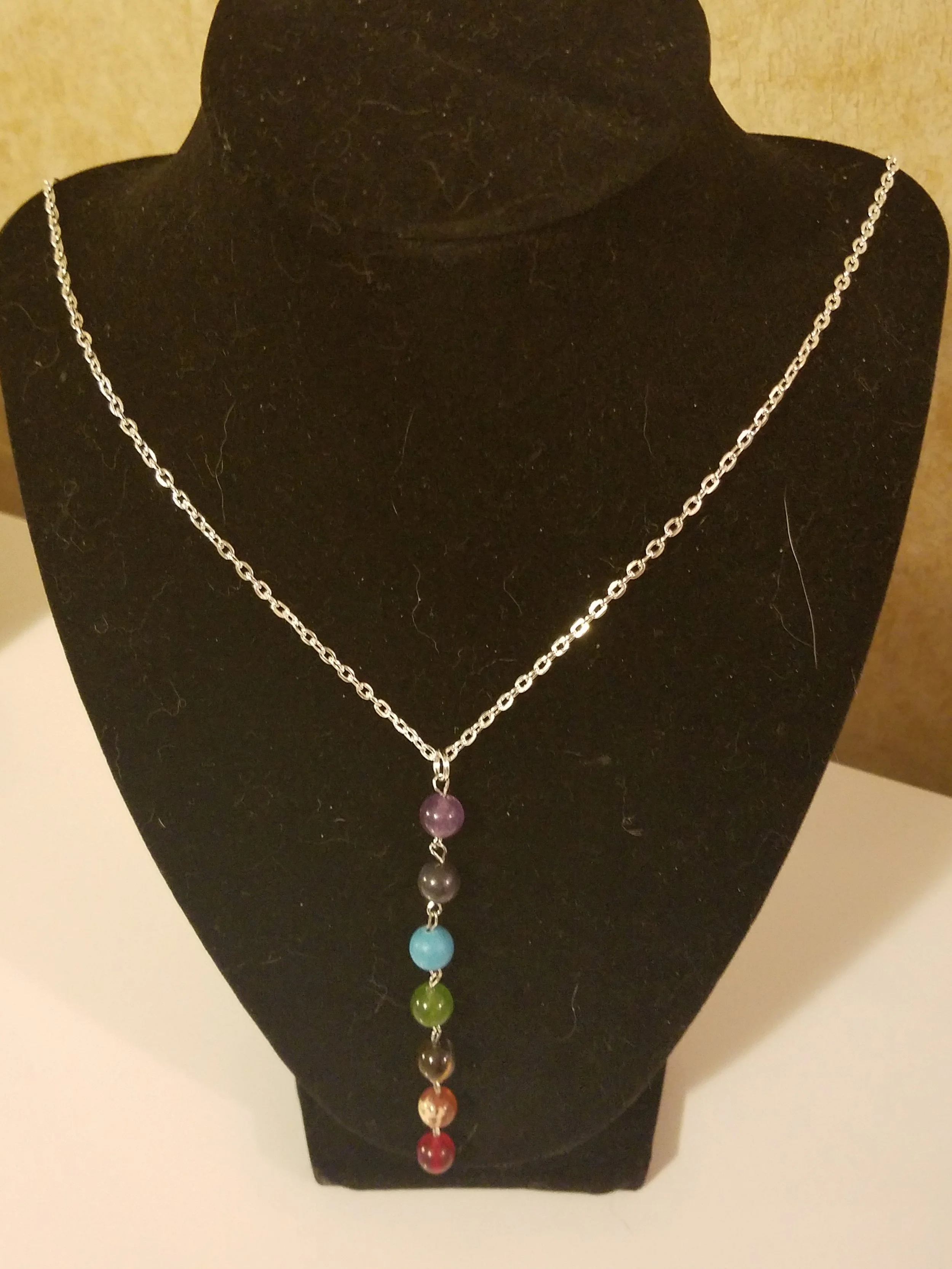 A silver chain necklace with a pendant that has seven colorful beads arranged vertically, each bead in a different color.