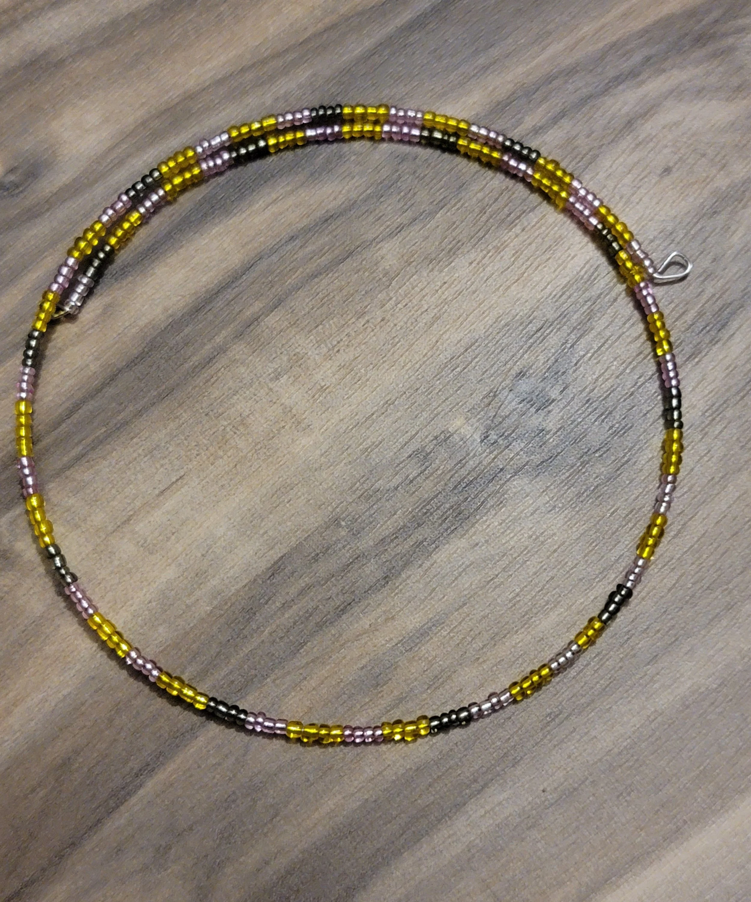 Colorful beaded necklace with black, gold, pink, and purple beads on a wooden surface.
