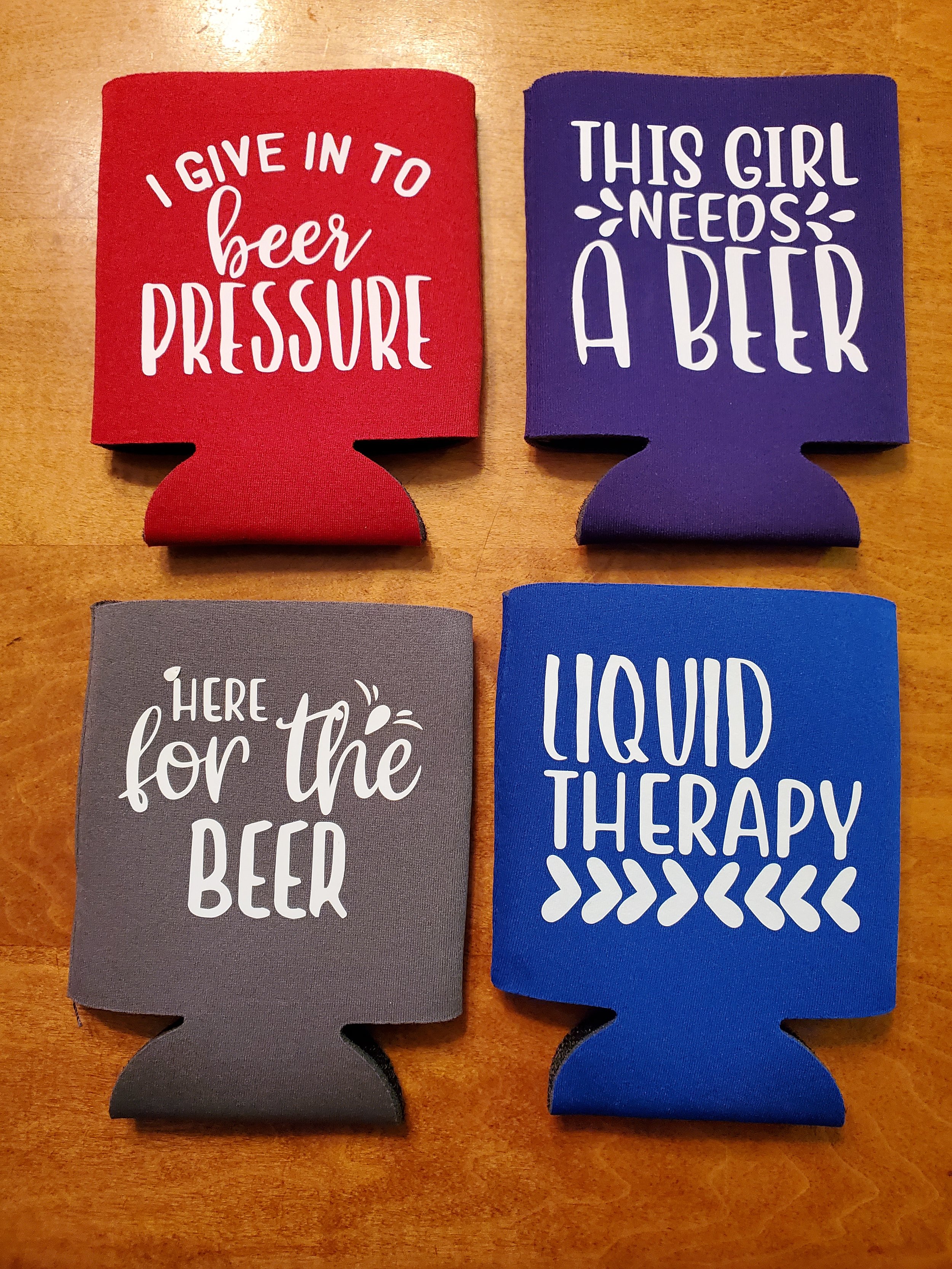 Four colorful drink koozies on a wooden surface with humorous beer-related sayings.