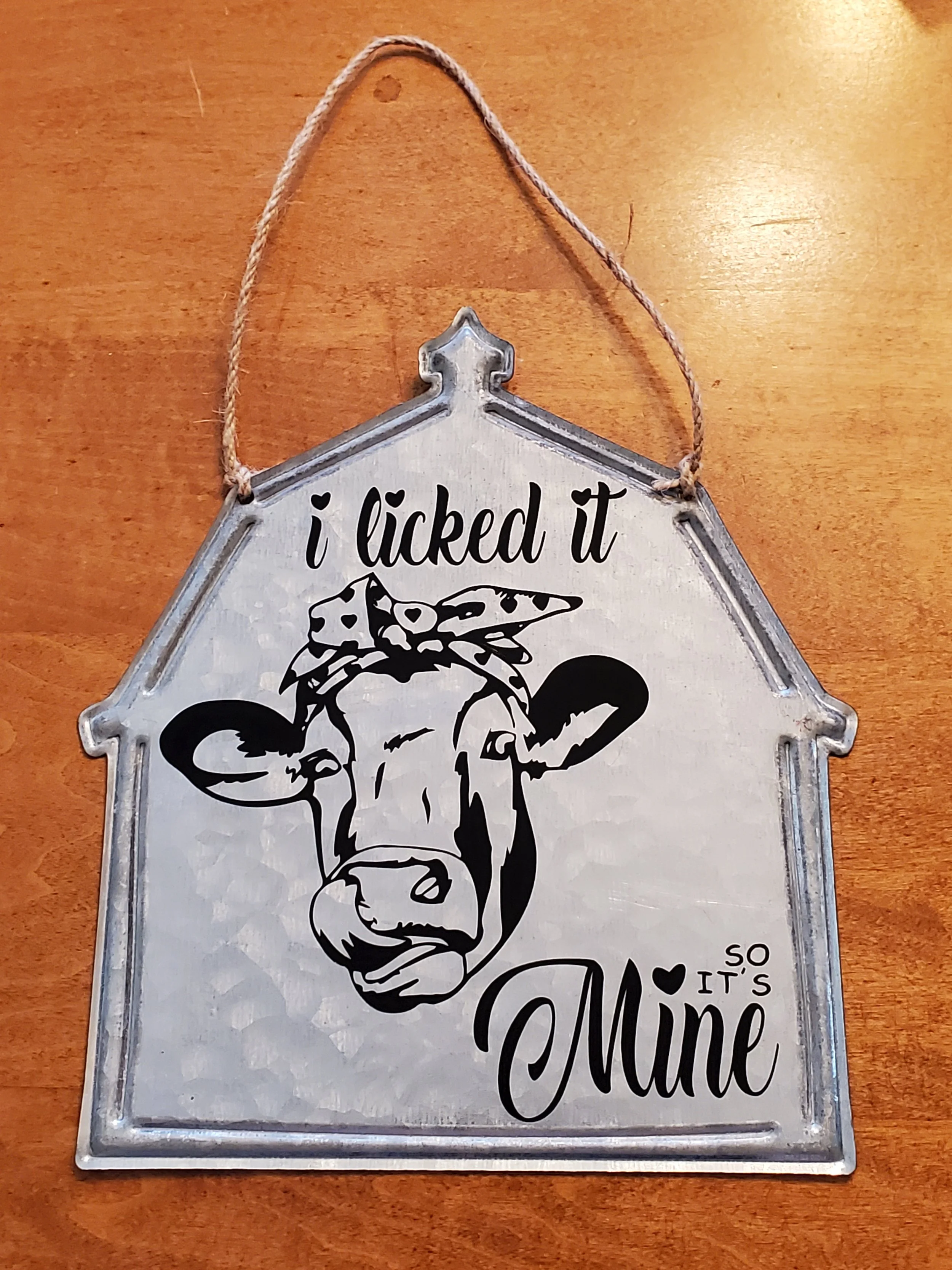 Decorative wall sign with a cow illustration and the phrase "I licked it so it's mine" on a wooden surface.