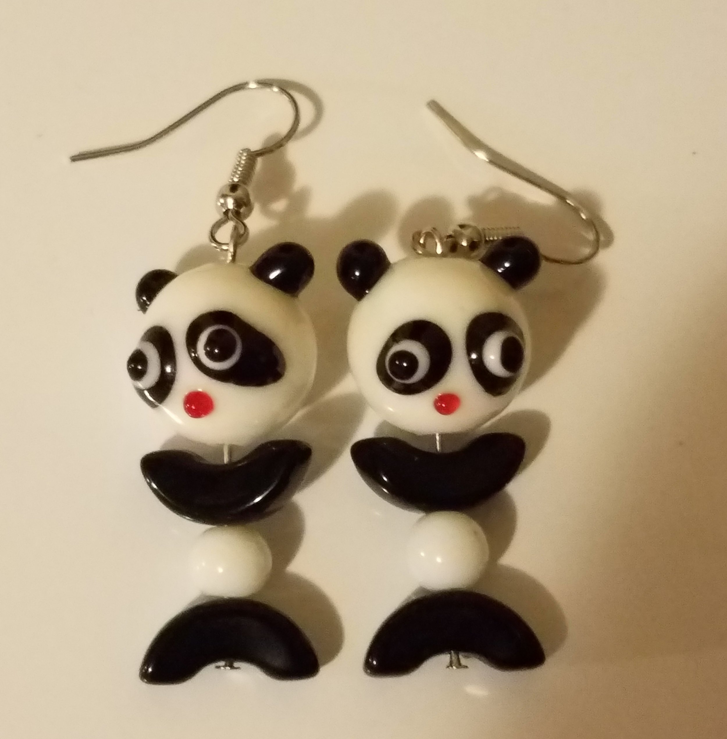 Panda-themed earrings with panda face and body in black and white, featuring red nose accents, on fishhook ear wires.
