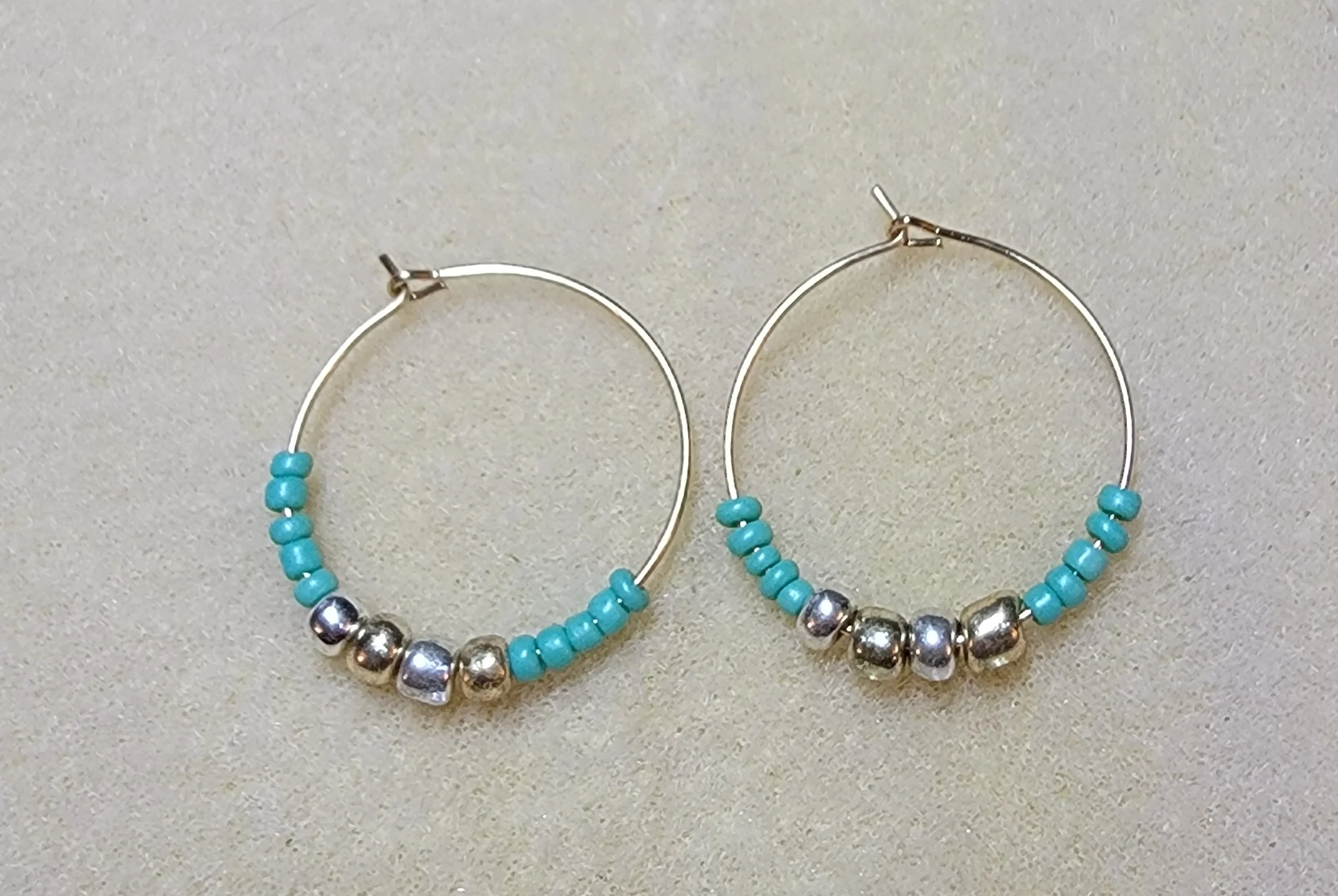 Pair of silver hoop earrings with turquoise beads and silver accents on a light-colored background.