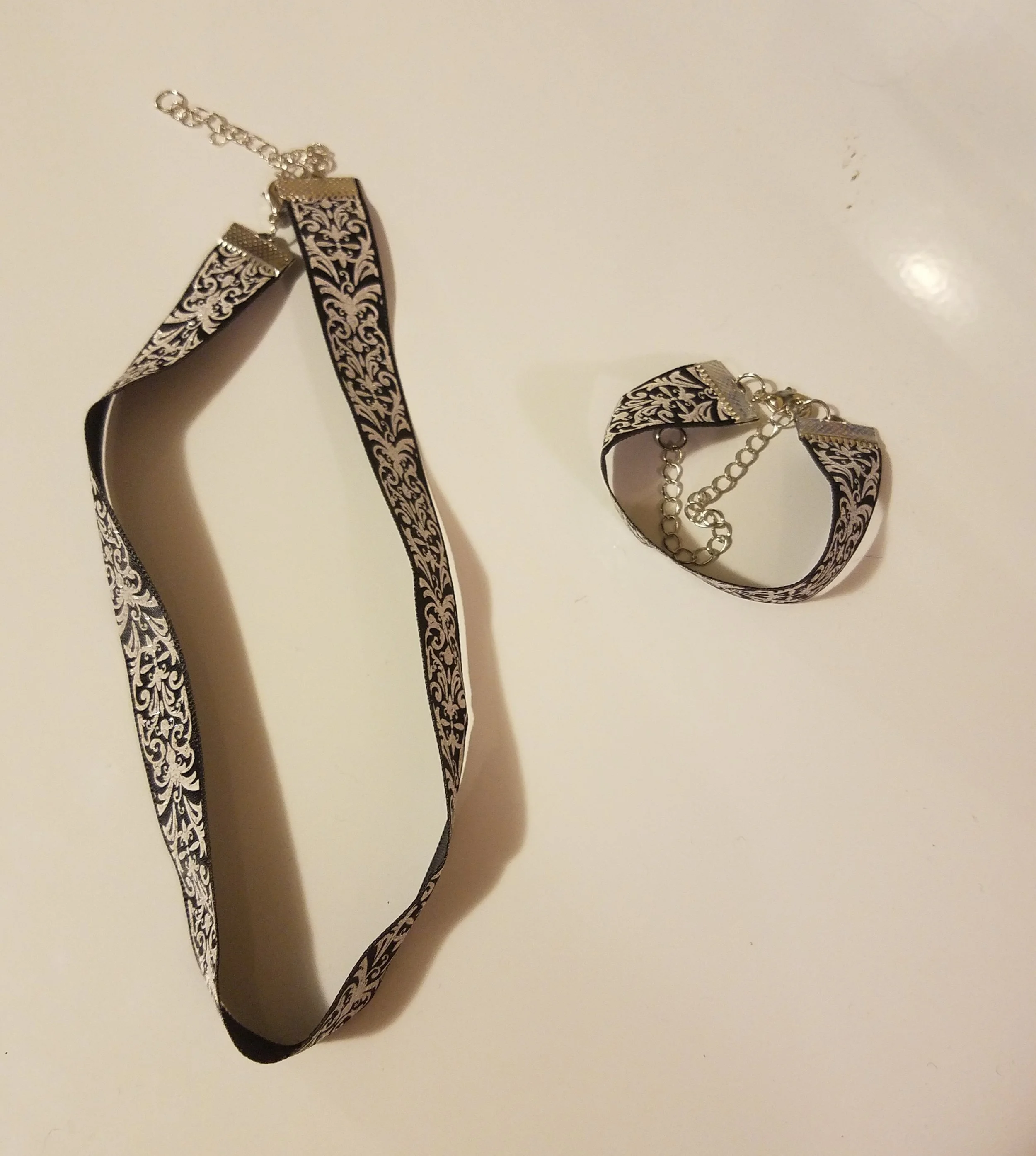 A black and white patterned choker necklace and matching bracelet with silver chain details on a white surface.