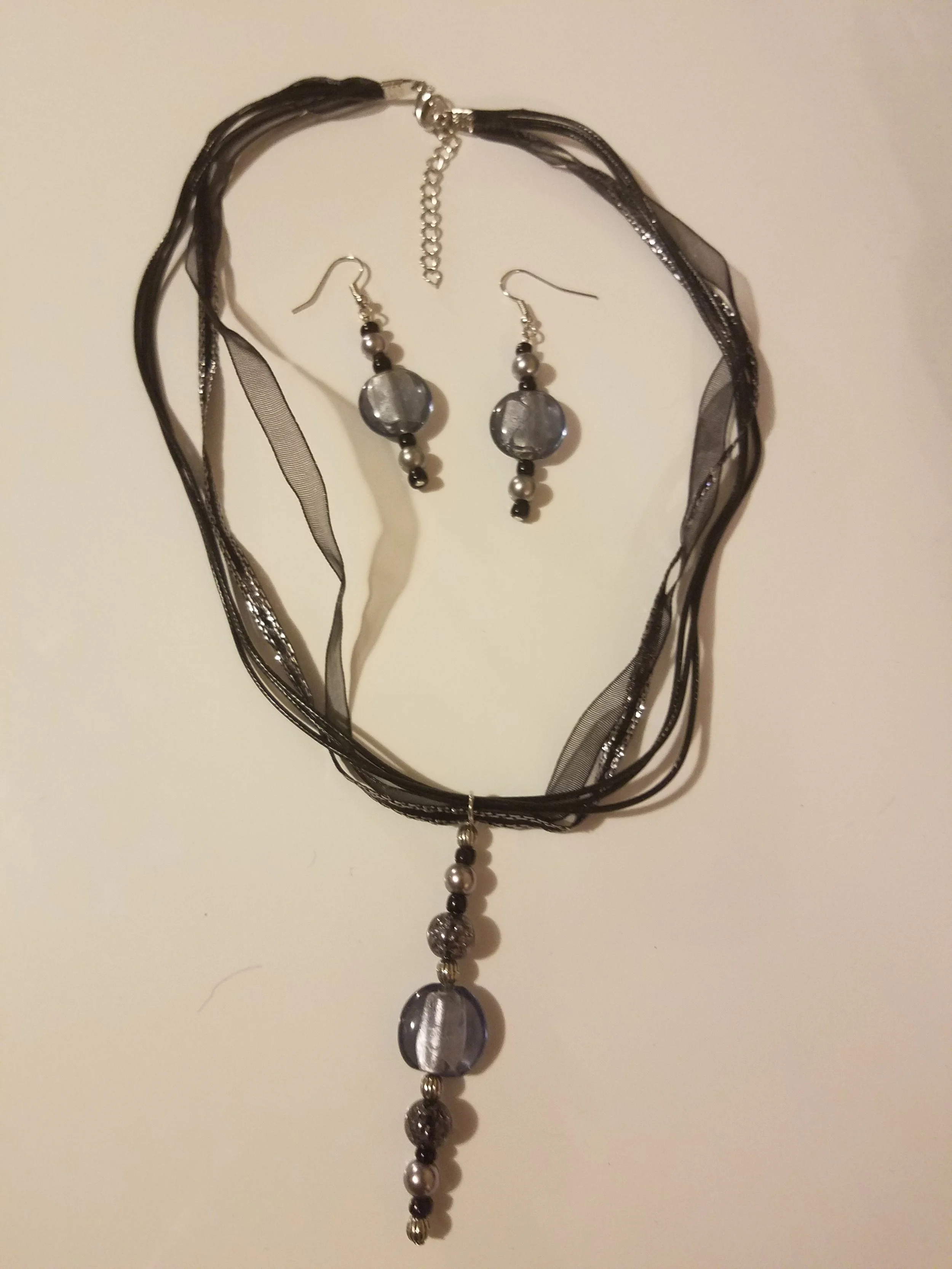 Set of jewelry including a black ribbon necklace, a pair of matching earrings, and a pendant necklace, all featuring black, gray, and silver beads.
