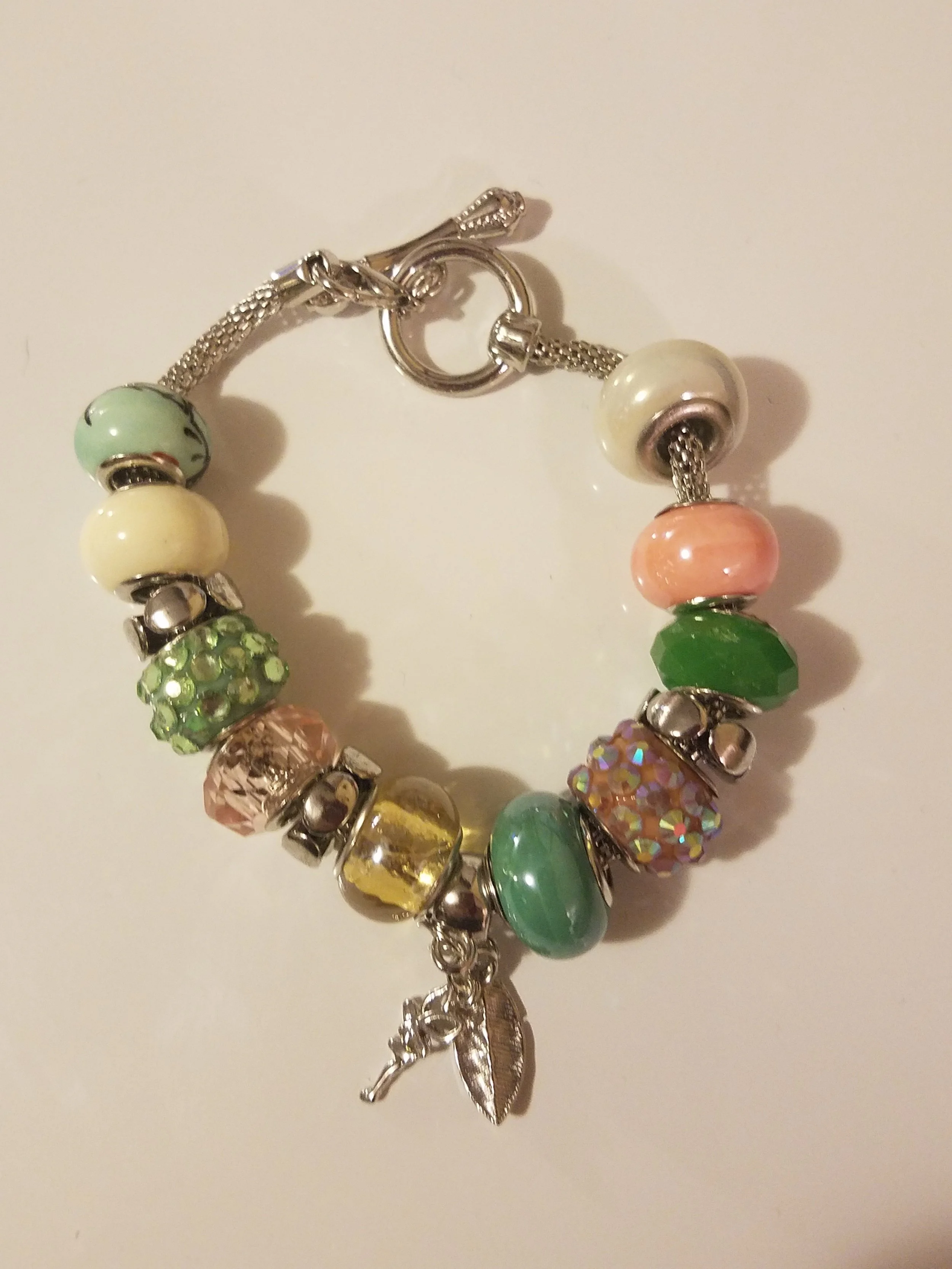 Colorful charm bracelet with various beads and a small leaf and bird charm.