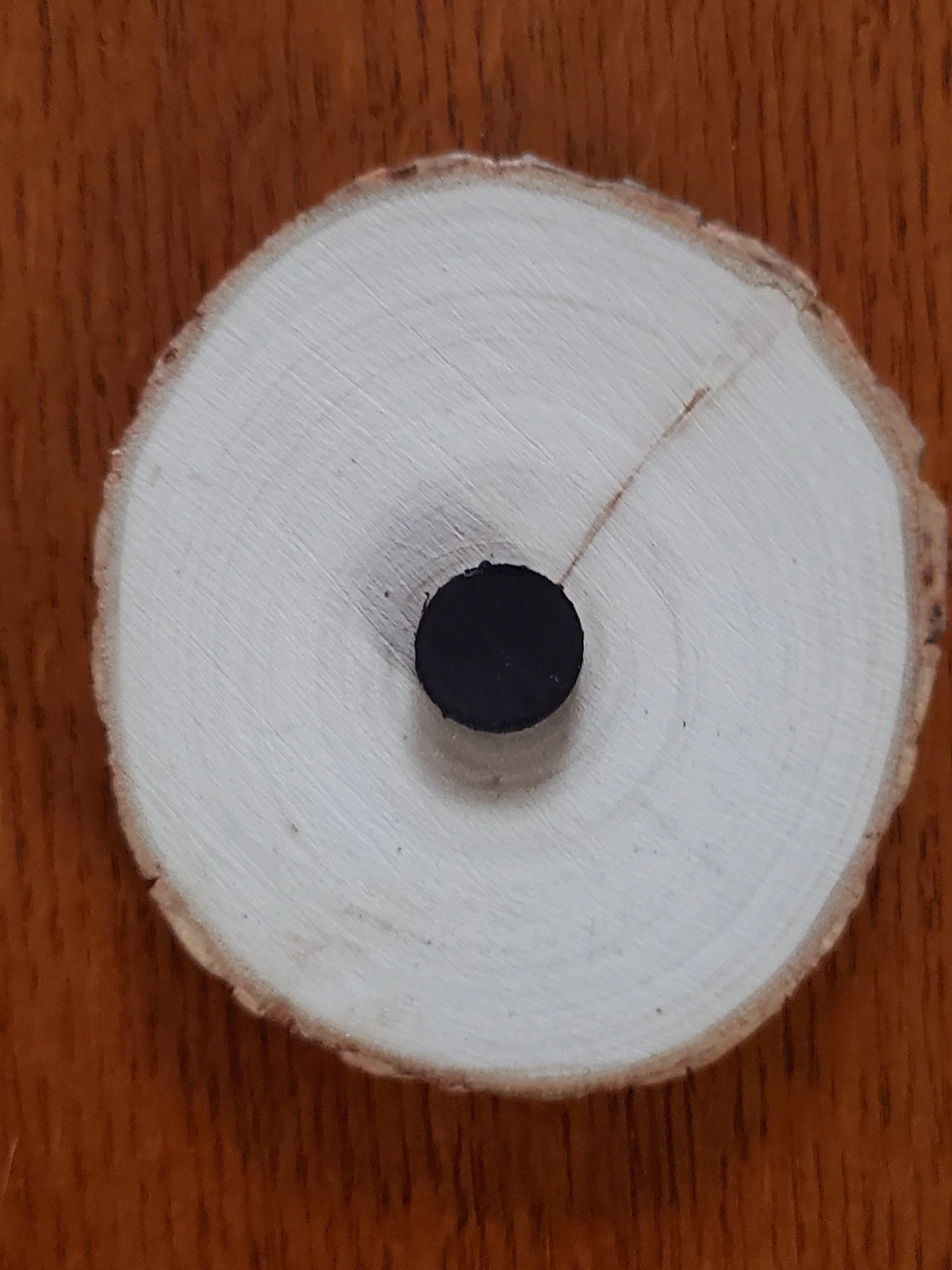 Close-up of a painted wooden disc with a black center, mounted on a wooden surface.