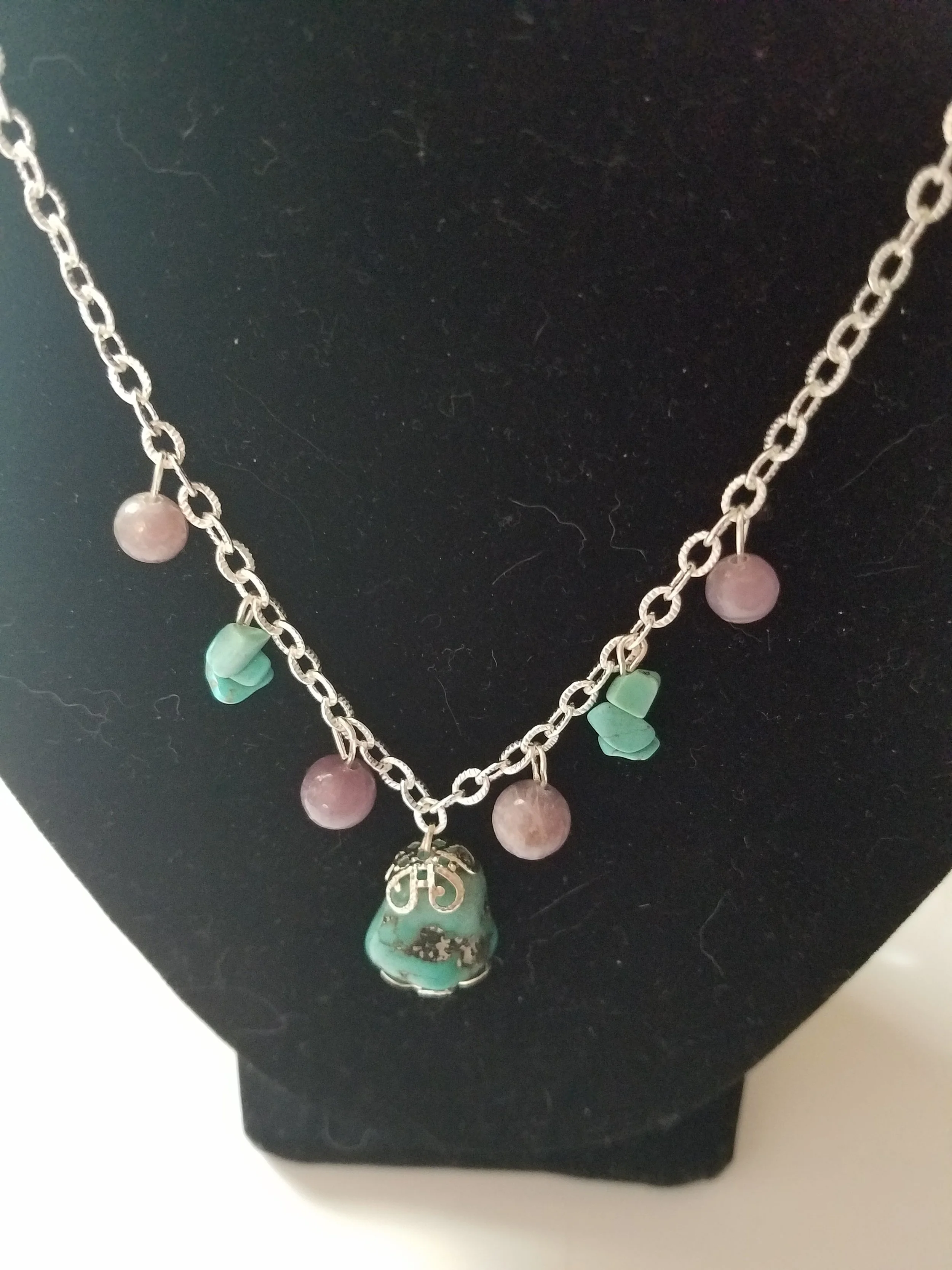 Silver necklace with pink, green, and turquoise beads displayed on a black bust display