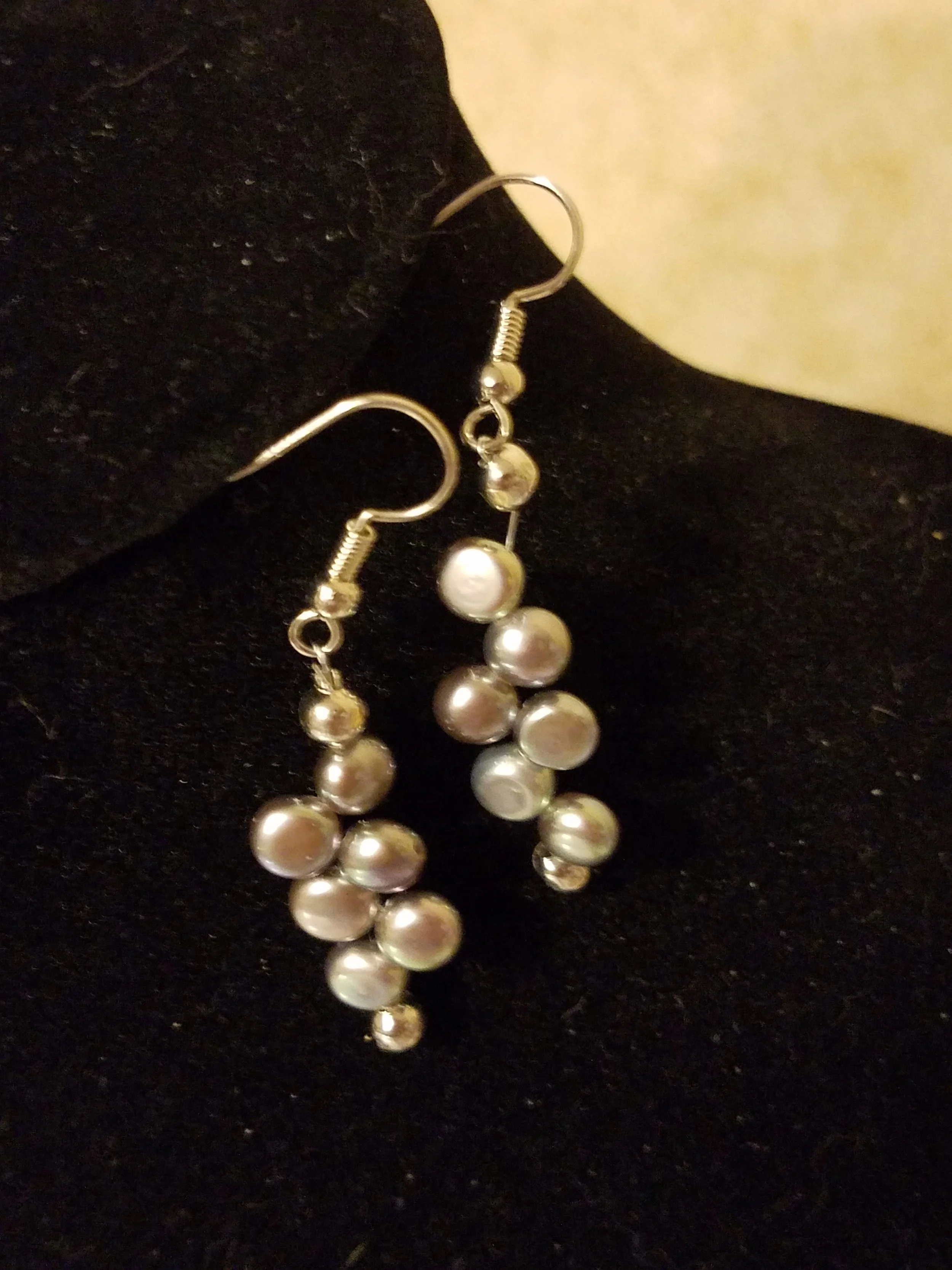 Silver earrings with multiple white pearls hanging on a black and white fabric background.