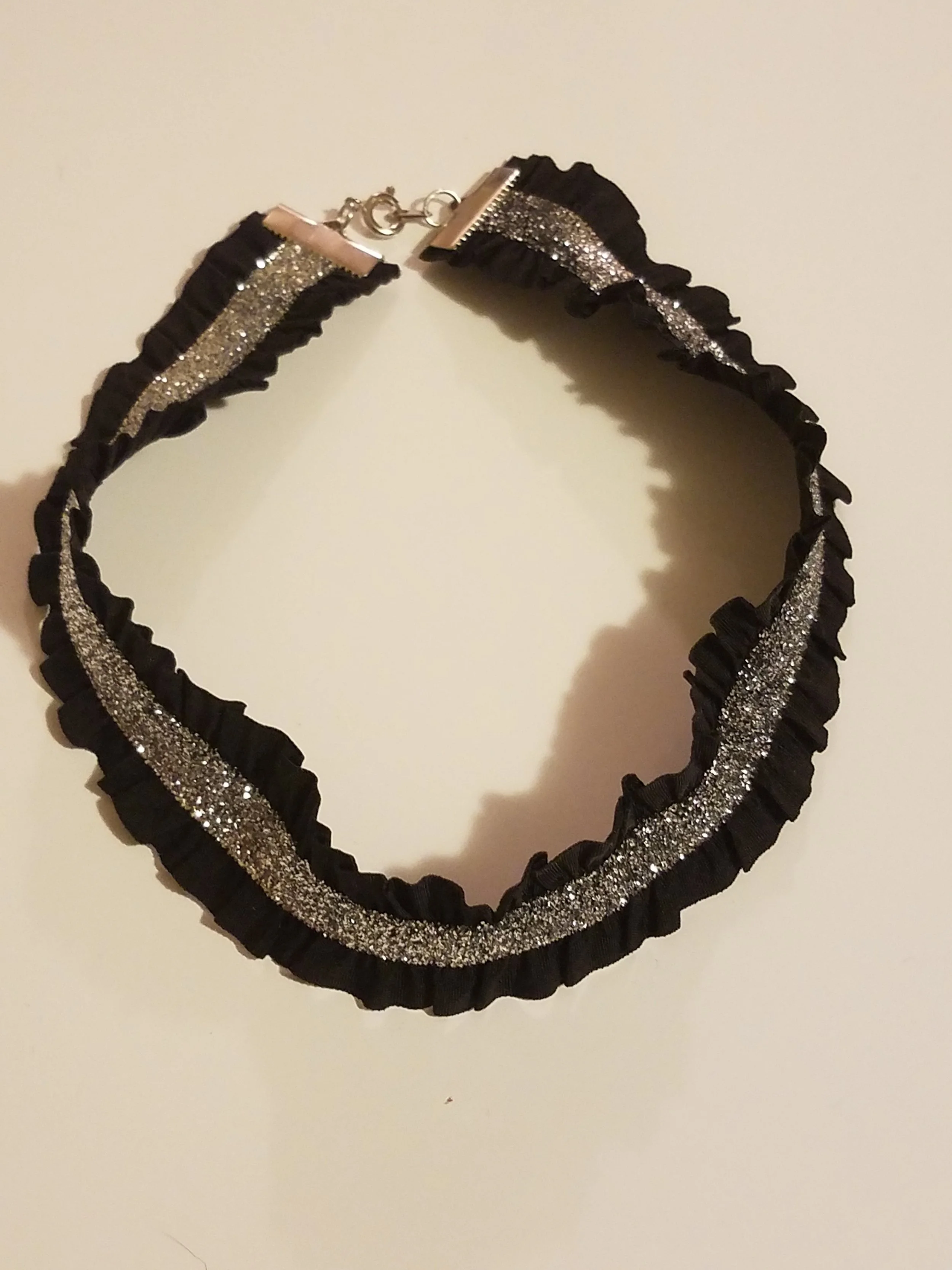 Black ruffled choker necklace with silver glittery stripe in the center.
