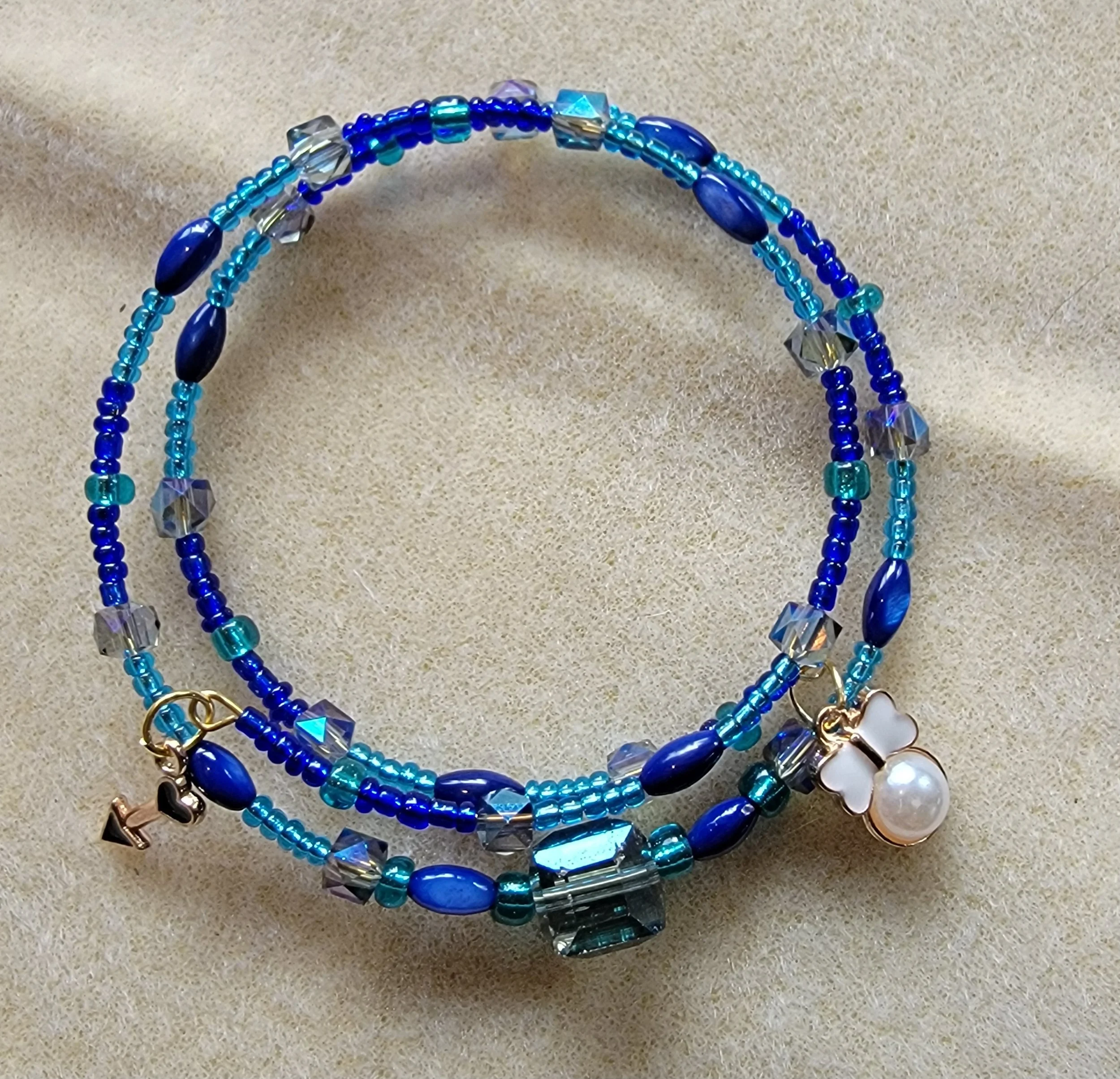Blue beaded jewelry with charms, including a pearl and a four-leaf clover