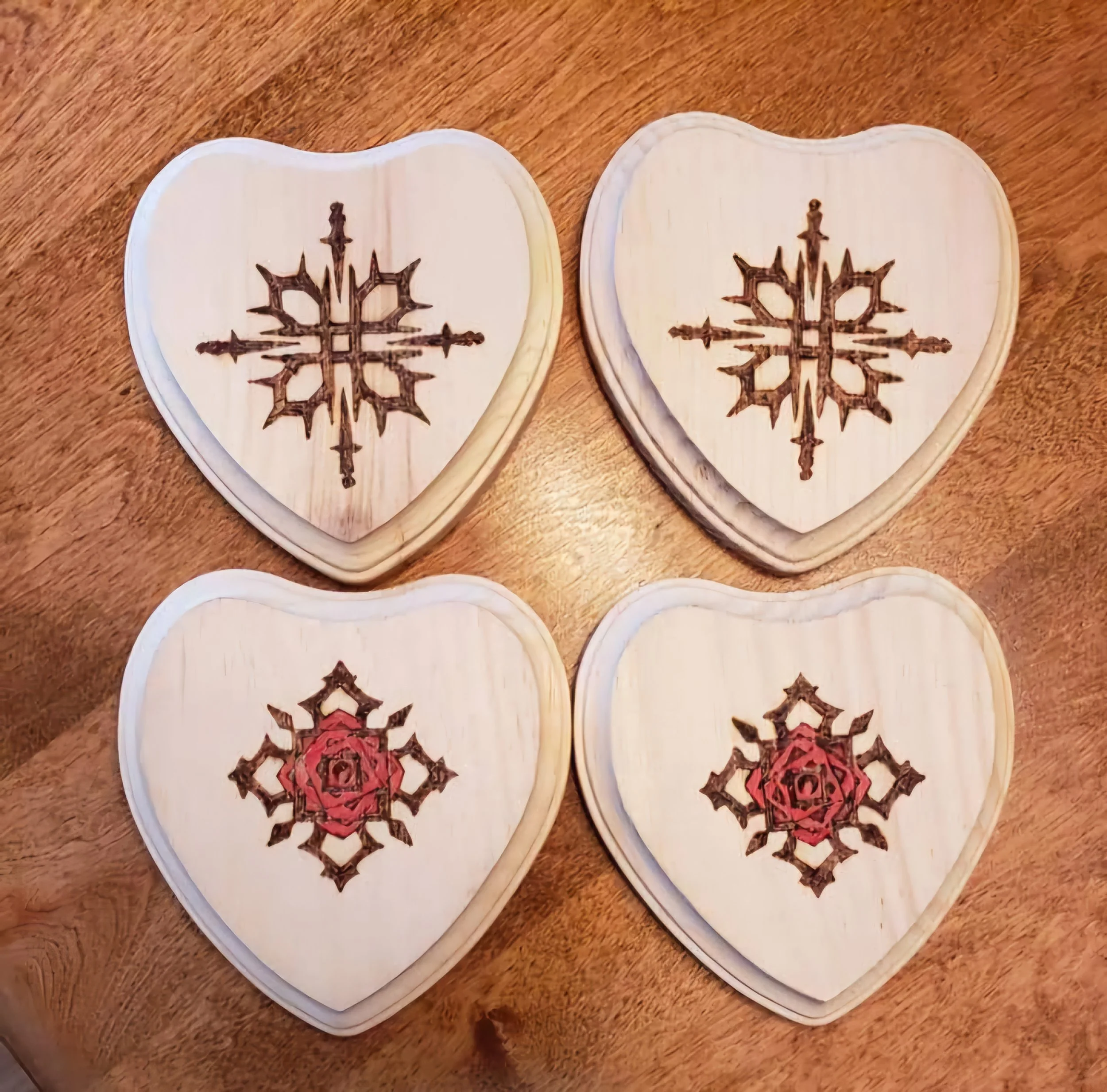 Four heart-shaped wood plaques with laser-engraved geometric snowflake designs, arranged on a wooden surface.