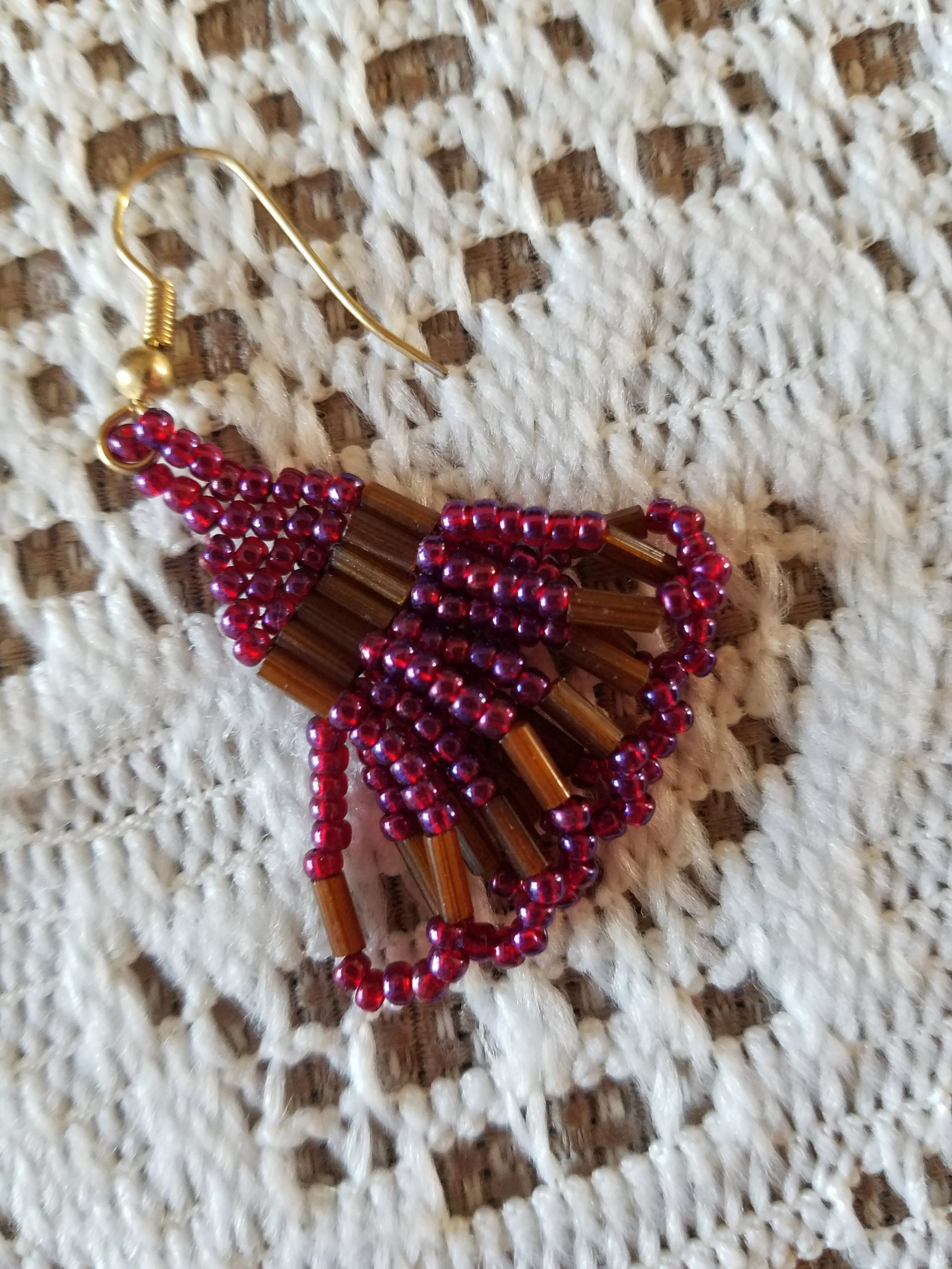 Beaded earring featuring brown and red beads, lying on a textured white fabric.