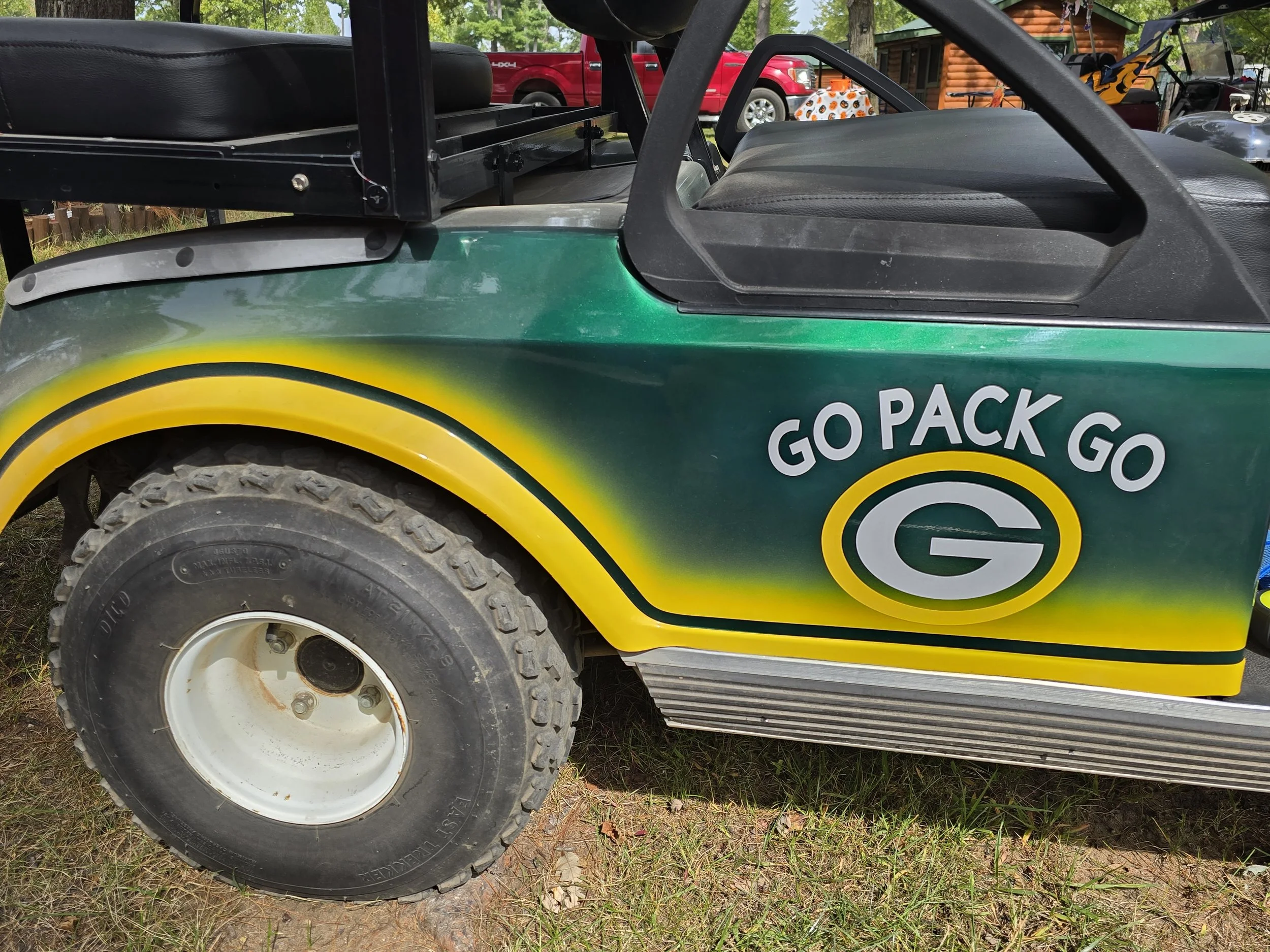 A golf cart decorated with green, yellow, and black paint featuring the Green Bay Packers logo and slogan 'Go Pack Go'.
