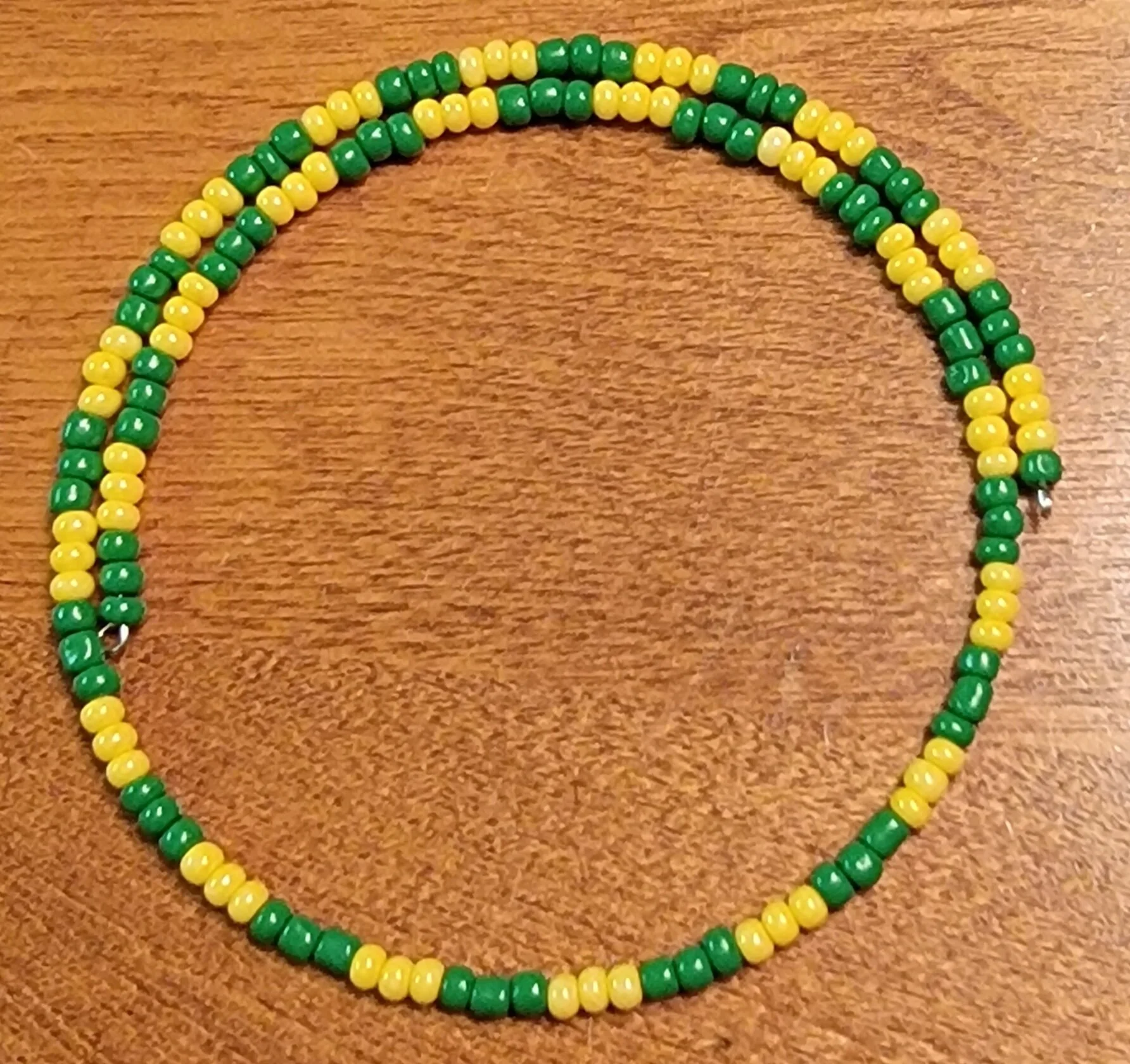 Beaded necklace with green and yellow beads on a wooden surface.