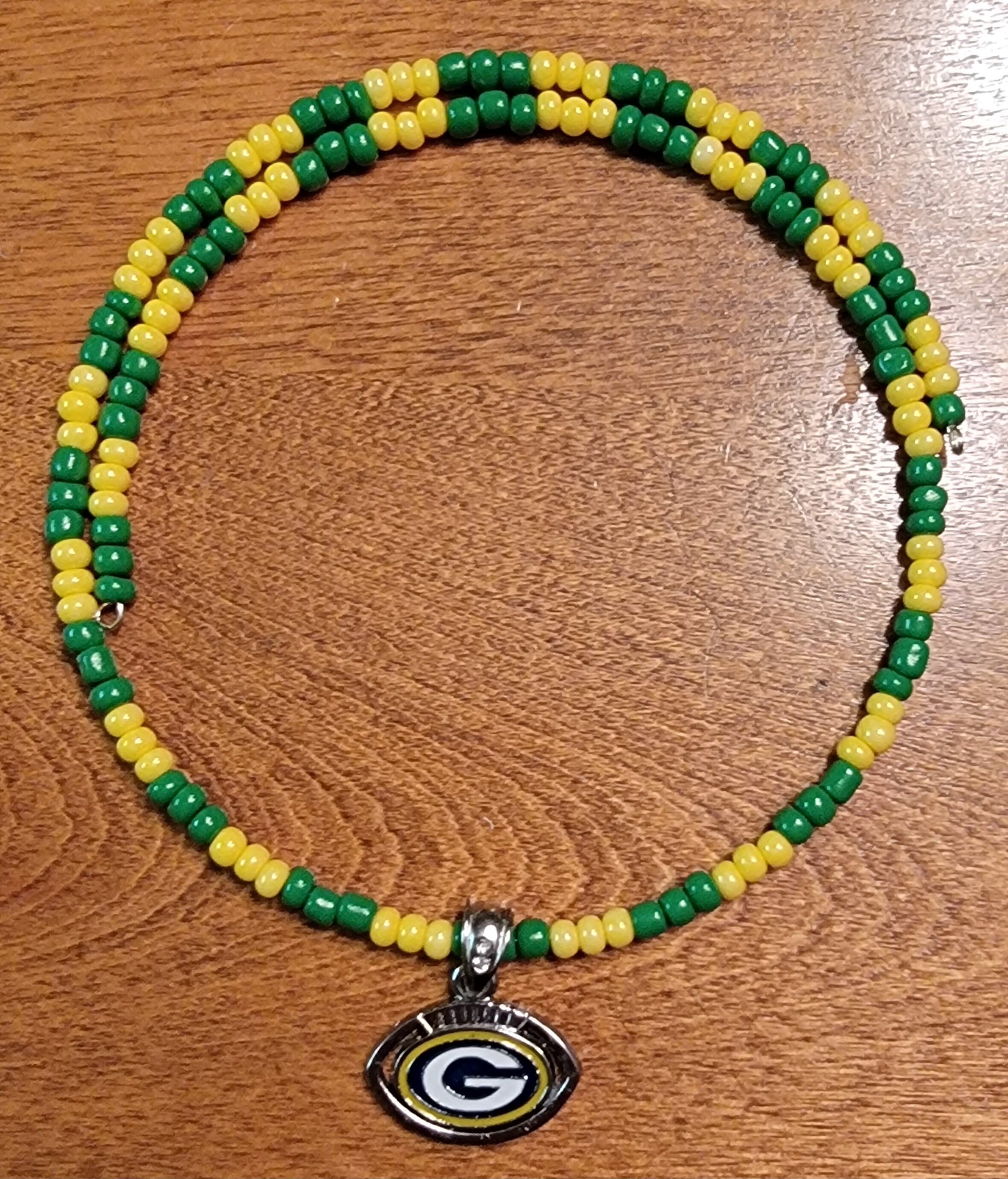 Green and yellow beaded necklace with a Green Bay Packers logo pendant on a wooden surface.