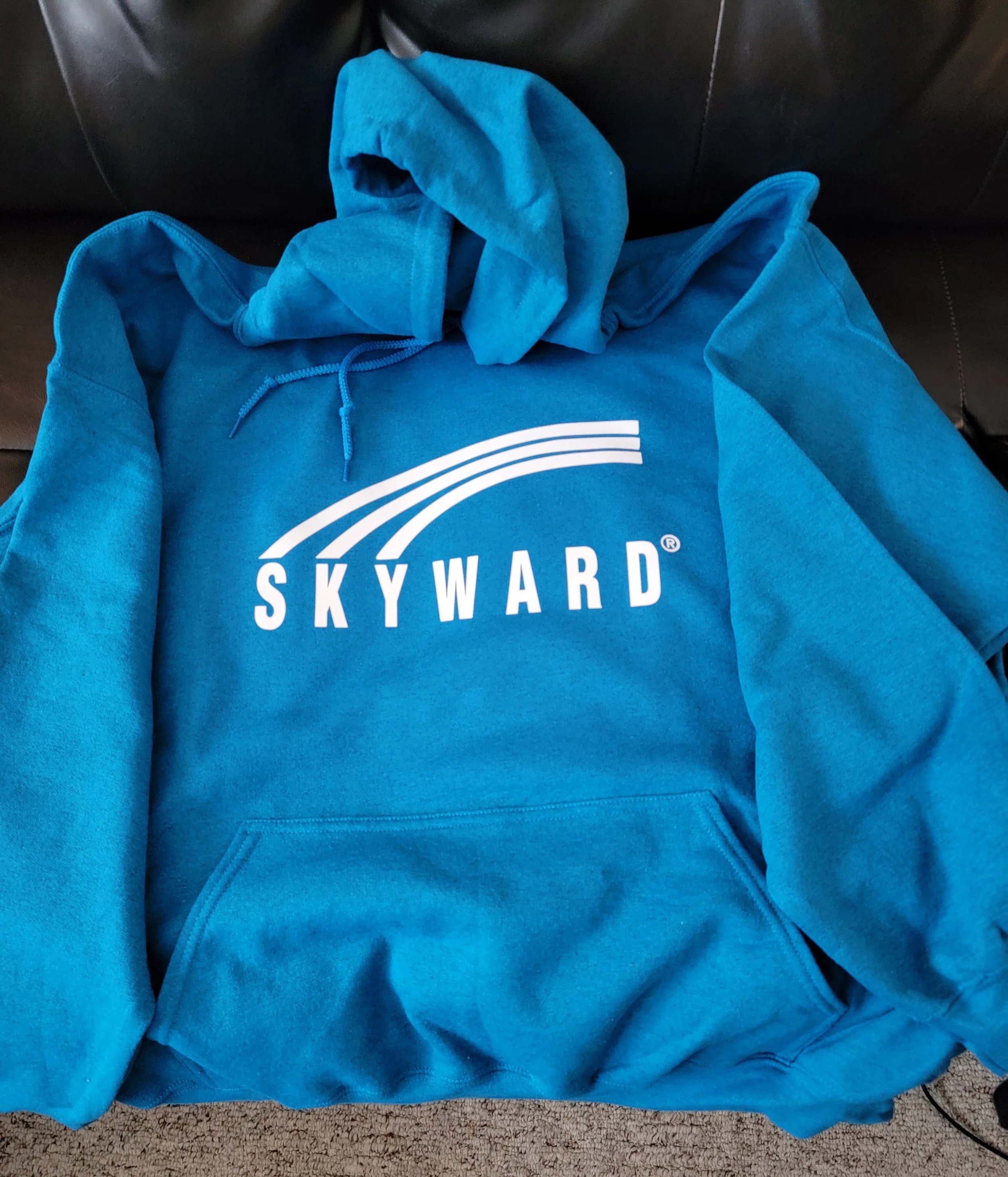 A blue hoodie with the Skyward logo on it, laid on a black couch.