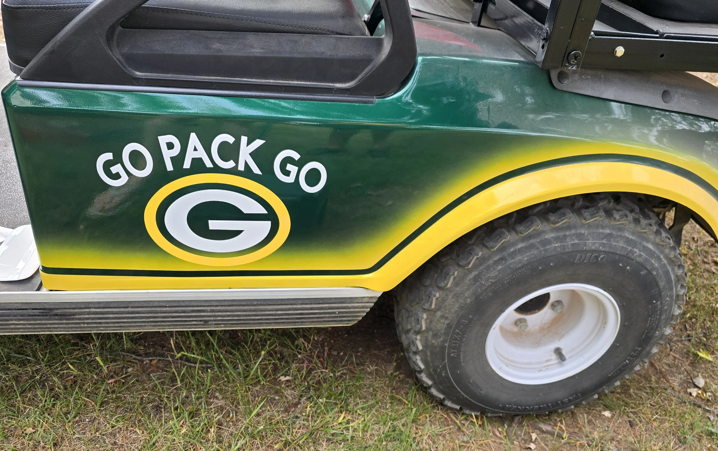 Close-up of a golf cart with Green Bay Packers branding, featuring the words 'GO PACK GO' and the Packers logo, parked on grass.