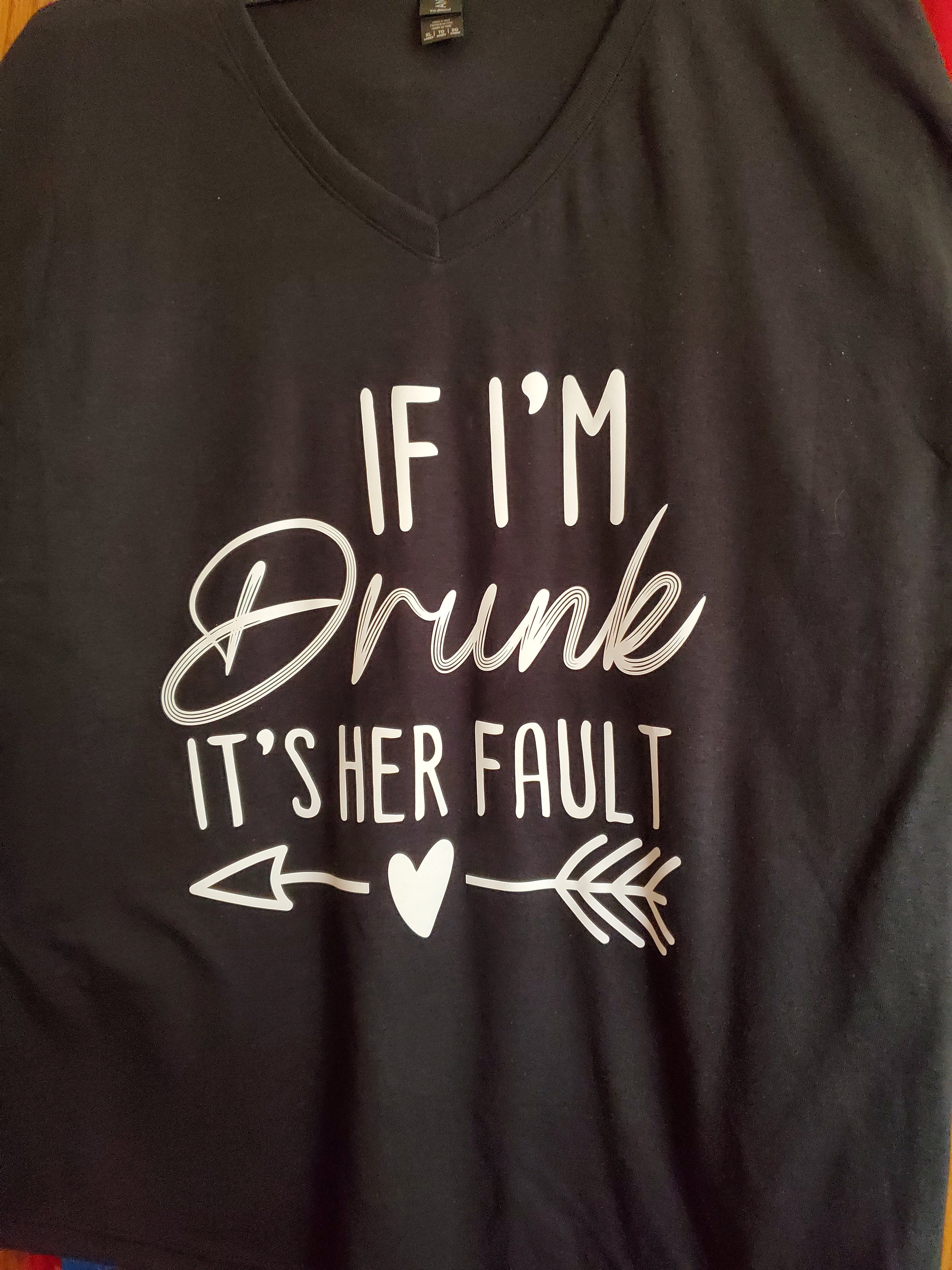 Black V-neck T-shirt with white text that says, "IF I'M Drunk IT'S HER FAULT," with a heart and arrow graphic.
