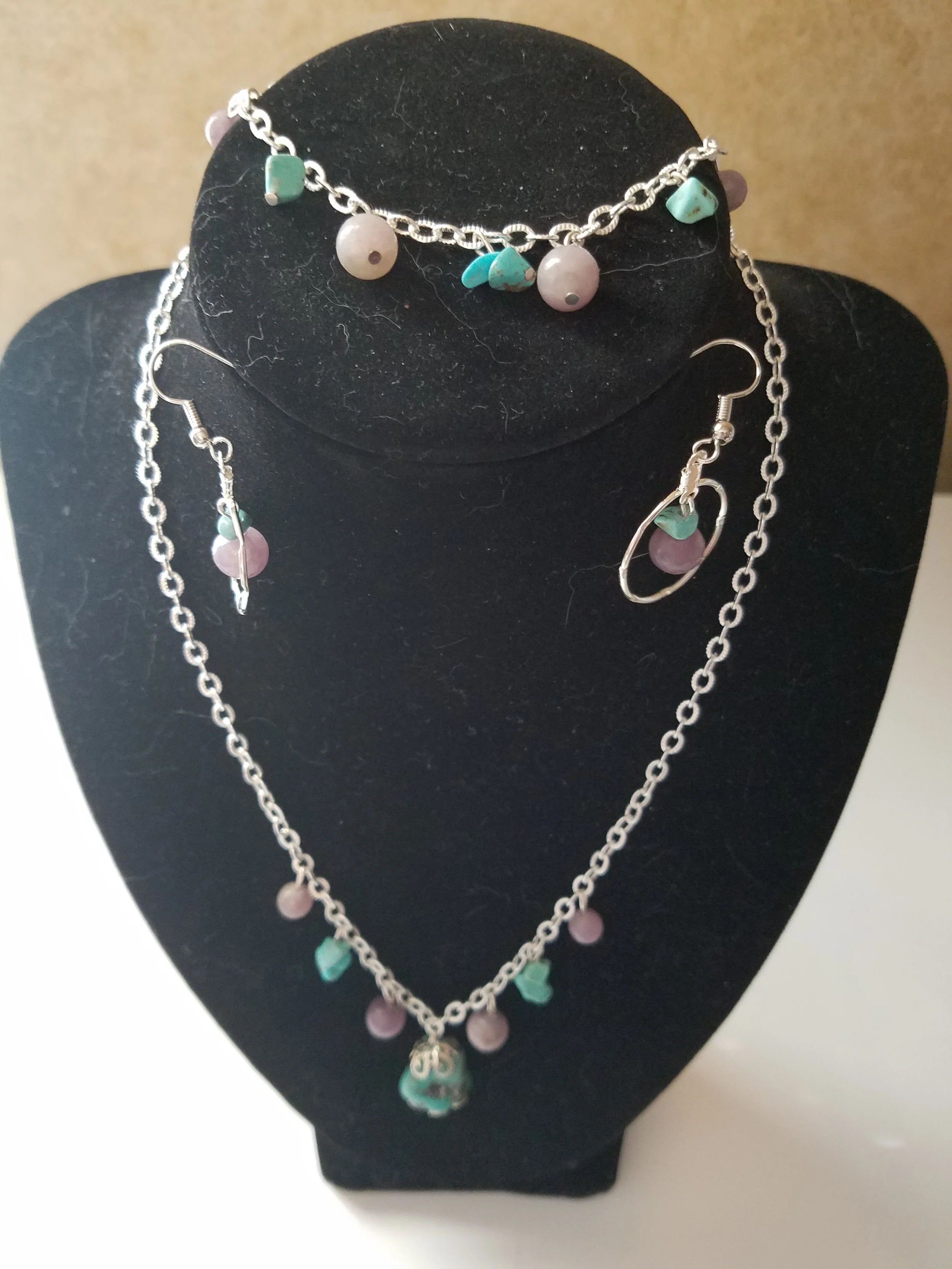 Jewelry set consisting of a necklace, bracelet, earrings, and ring with pink beads and turquoise stones displayed on a black jewelry stand.