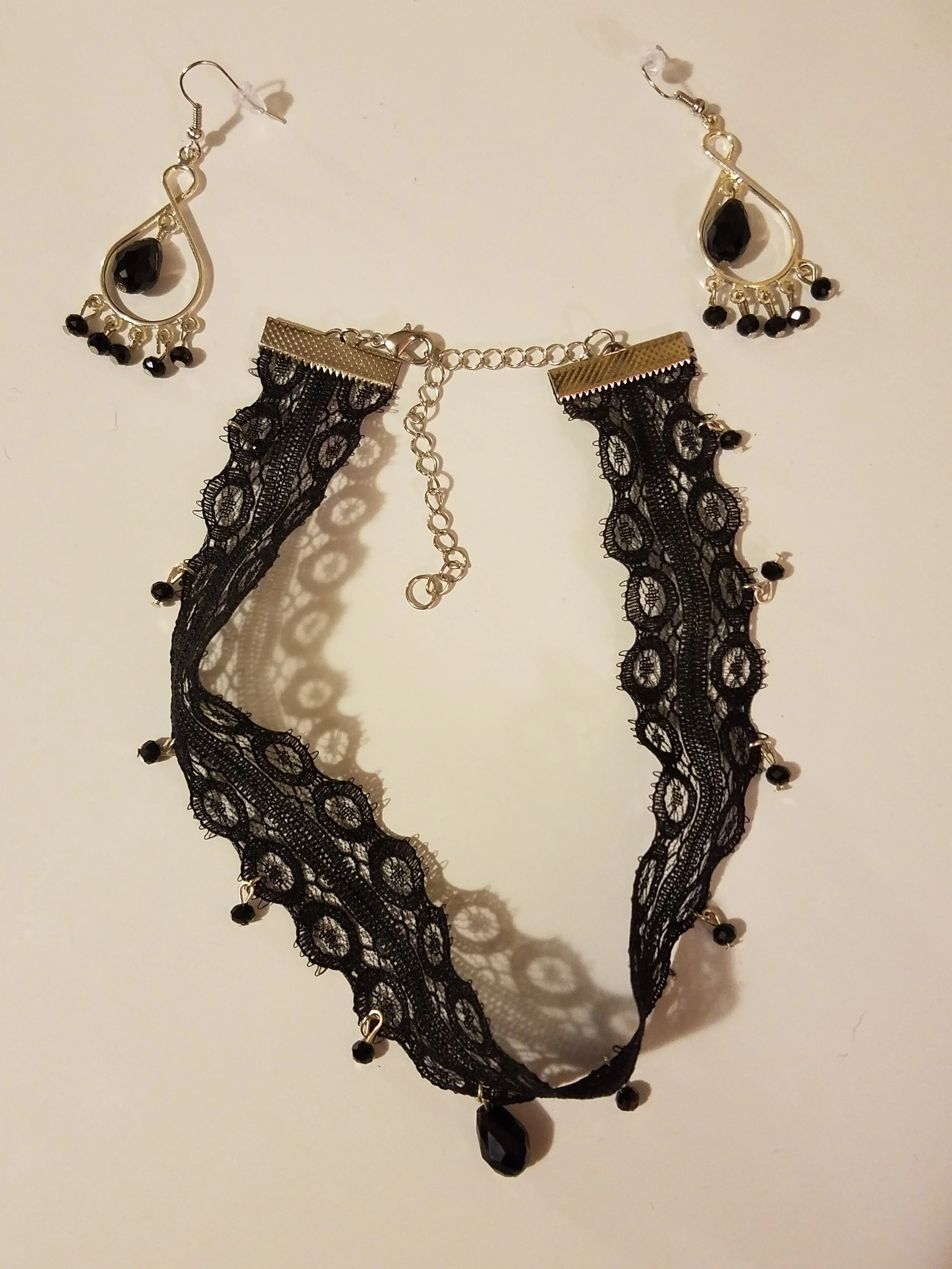 Black lace choker necklace with black teardrop pendant and earrings with black stones and gold accents.
