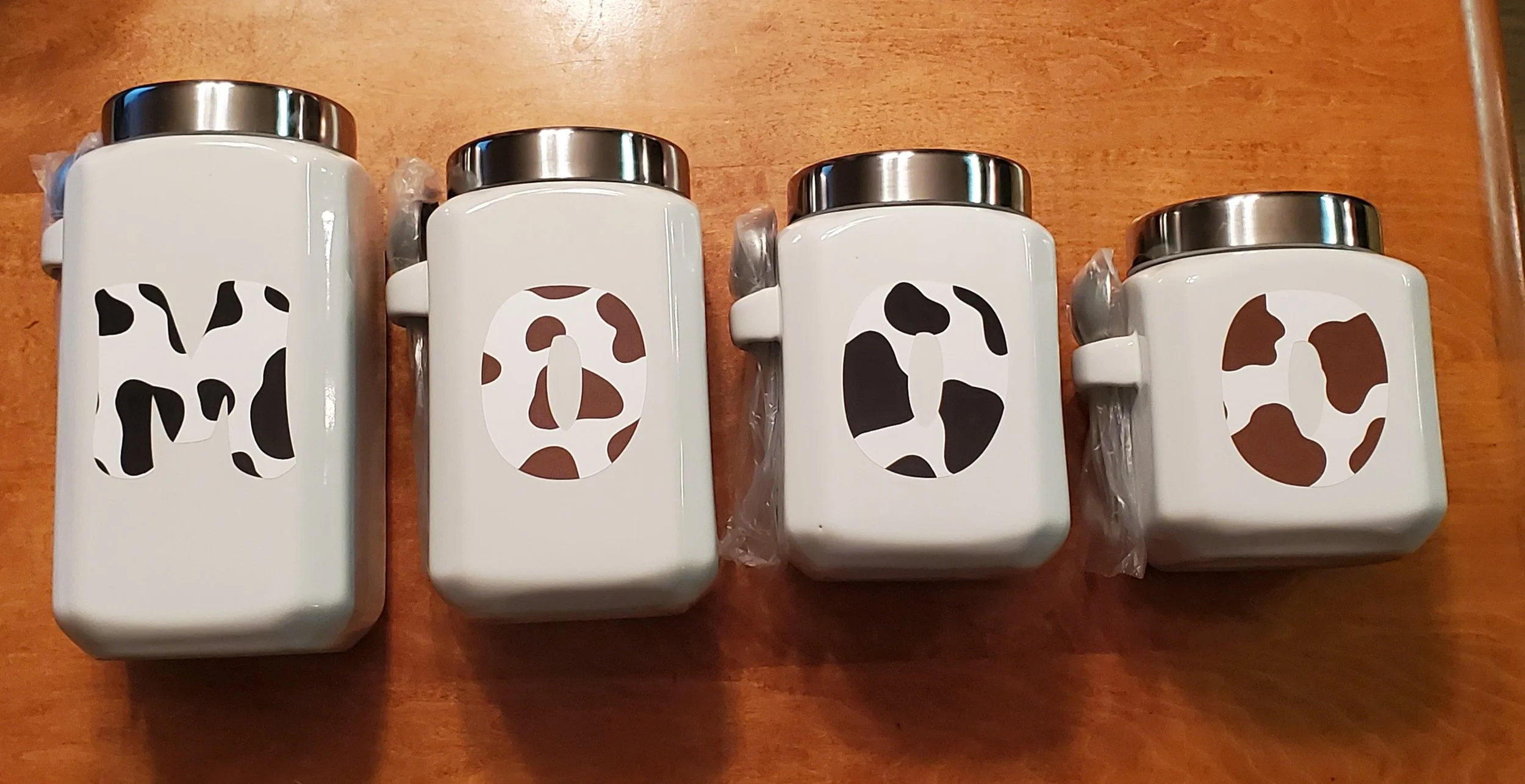 Four white containers with animal print labels spelling out 'MOOSE' on a wooden surface.