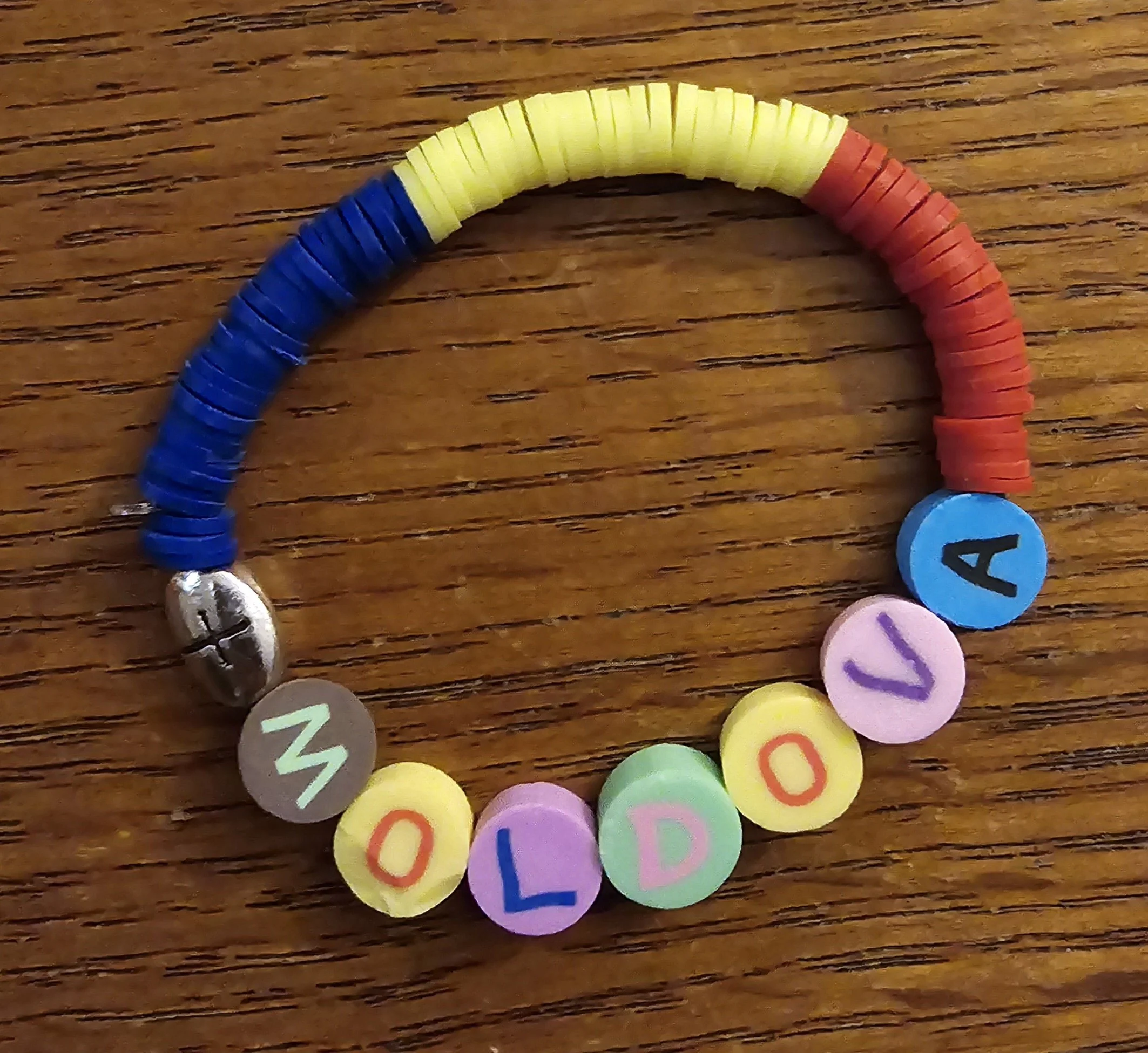 Colorful bracelet spelling out 'MOLDOVA' with letter beads and small colored discs on a wooden surface.