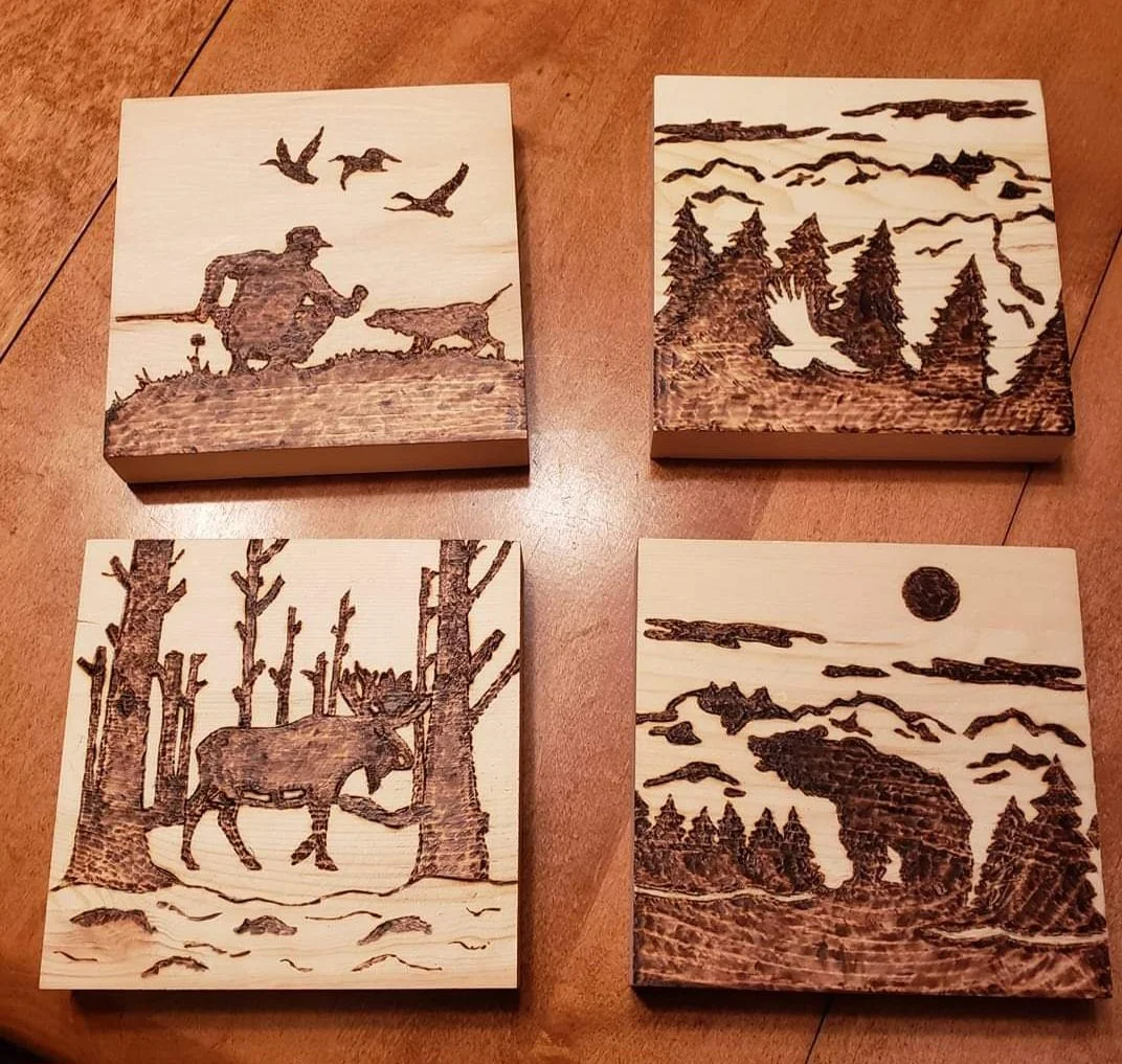 Set of four woodburned art pieces depicting outdoor wilderness scenes and wildlife.